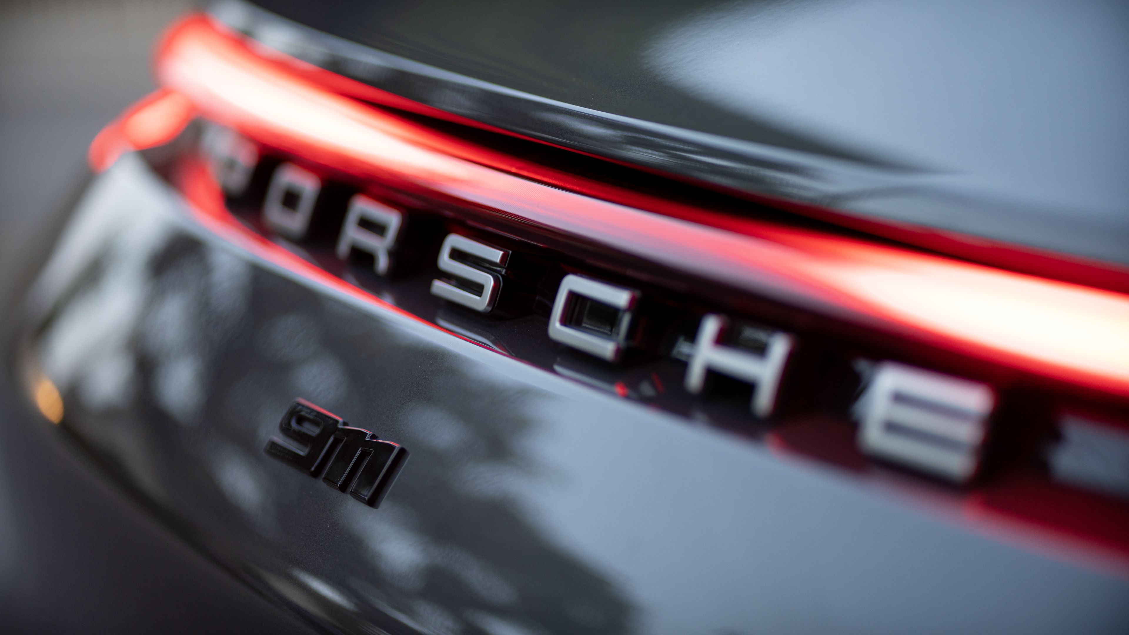 Close-up of the Porsche 911 logo and rear light design on a dark-colored vehicle.