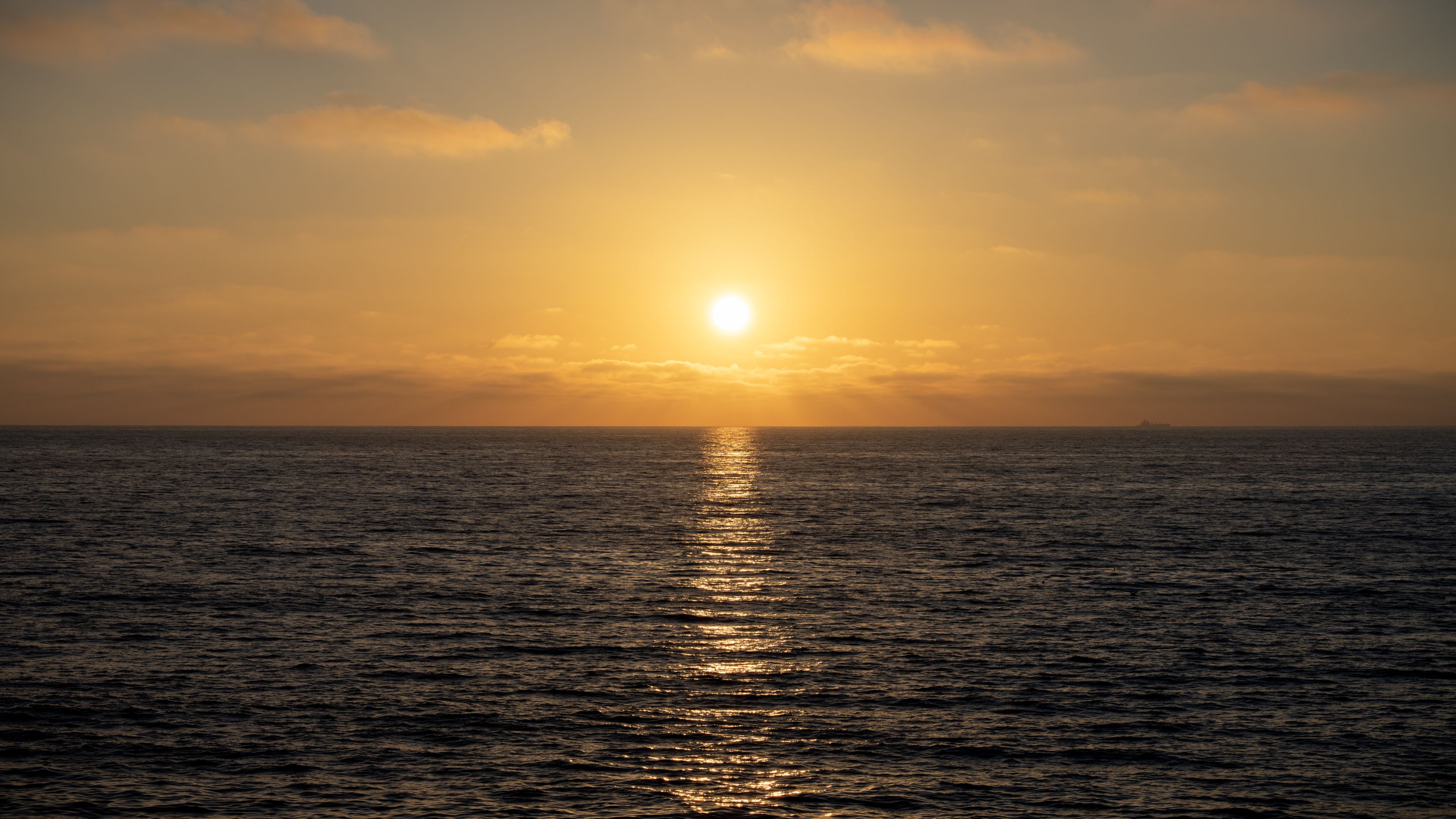 The sun sets over a calm ocean, with reflections visible in the water.