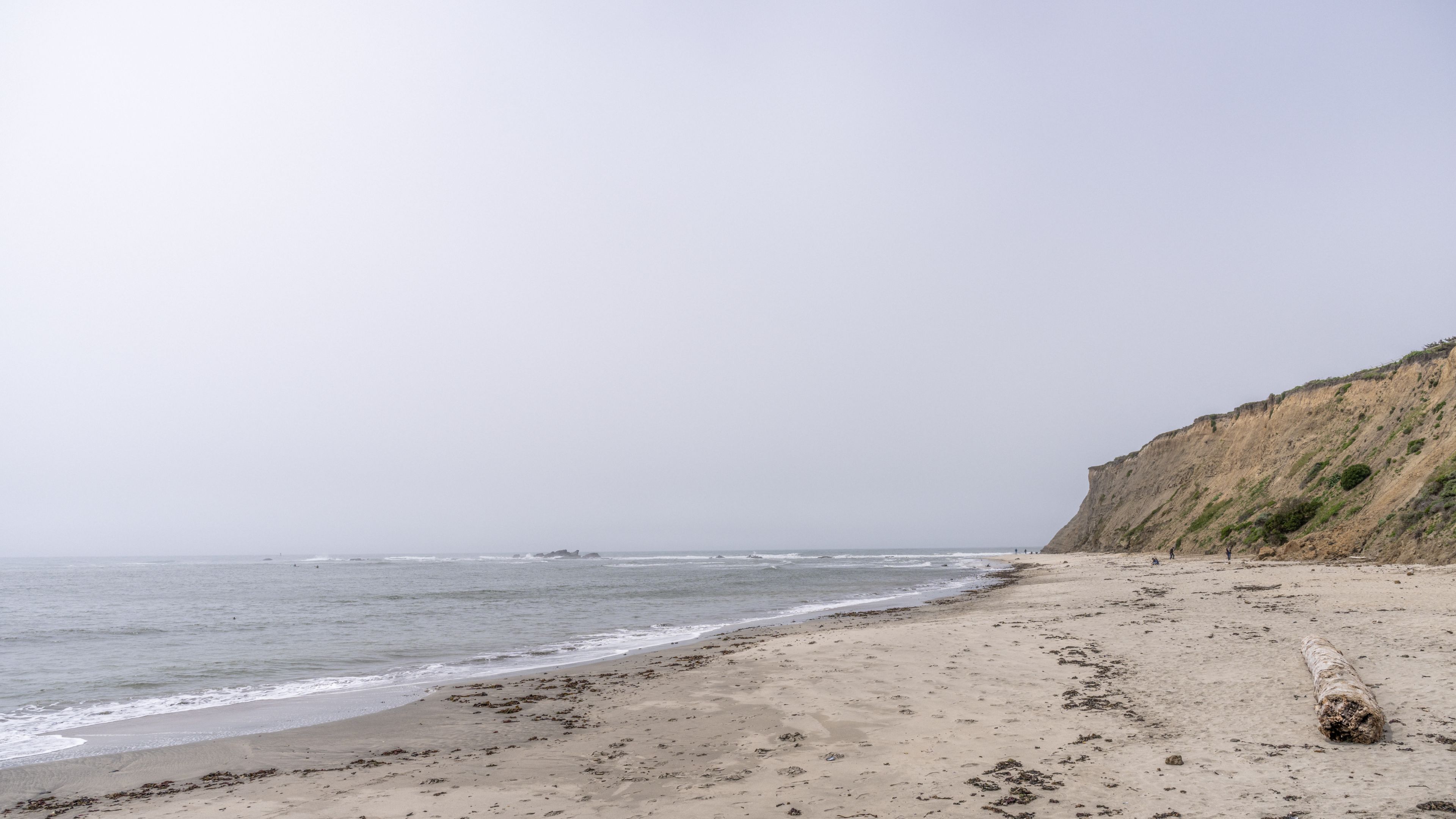 A sandy beach stretches alongside a rocky shoreline under overcast skies with waves lapping at the shore.