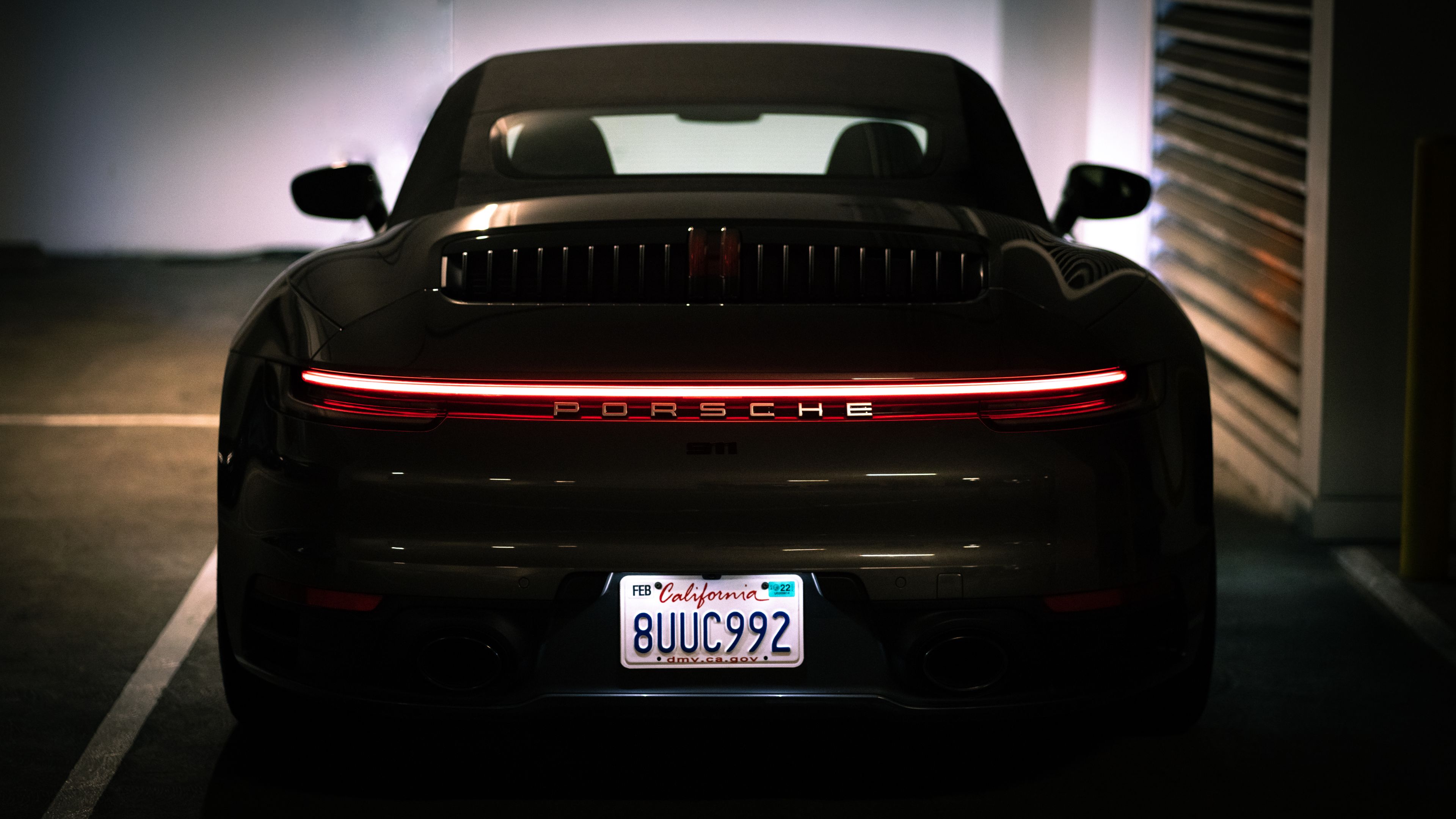 A Porsche sports car is parked in a dimly lit garage, showcasing its rear design and license plate.
