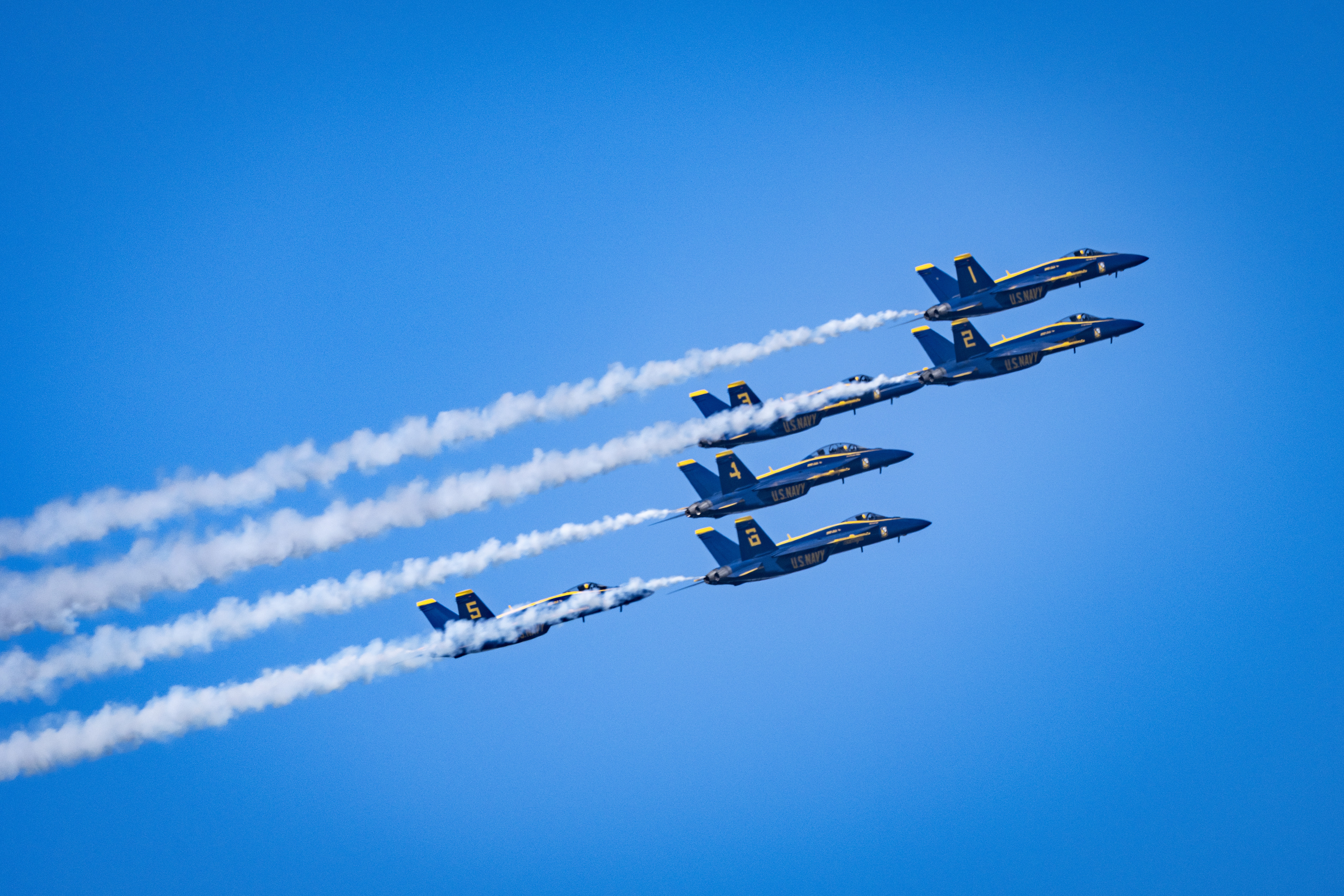 Blue Angels jets fly closely together with long white smoke trails behind them.