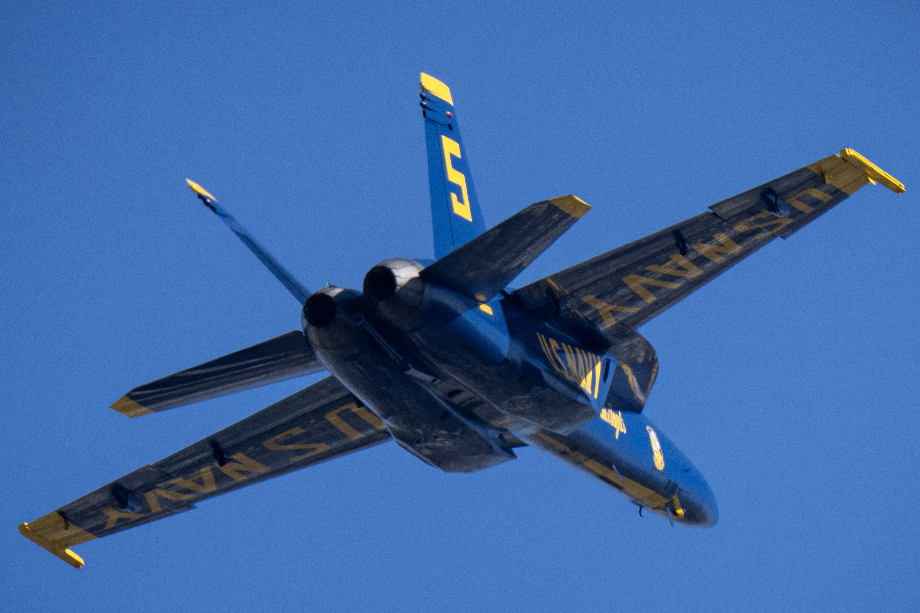 A Blue Angels jet passes overhead, seen from just behind its tail.