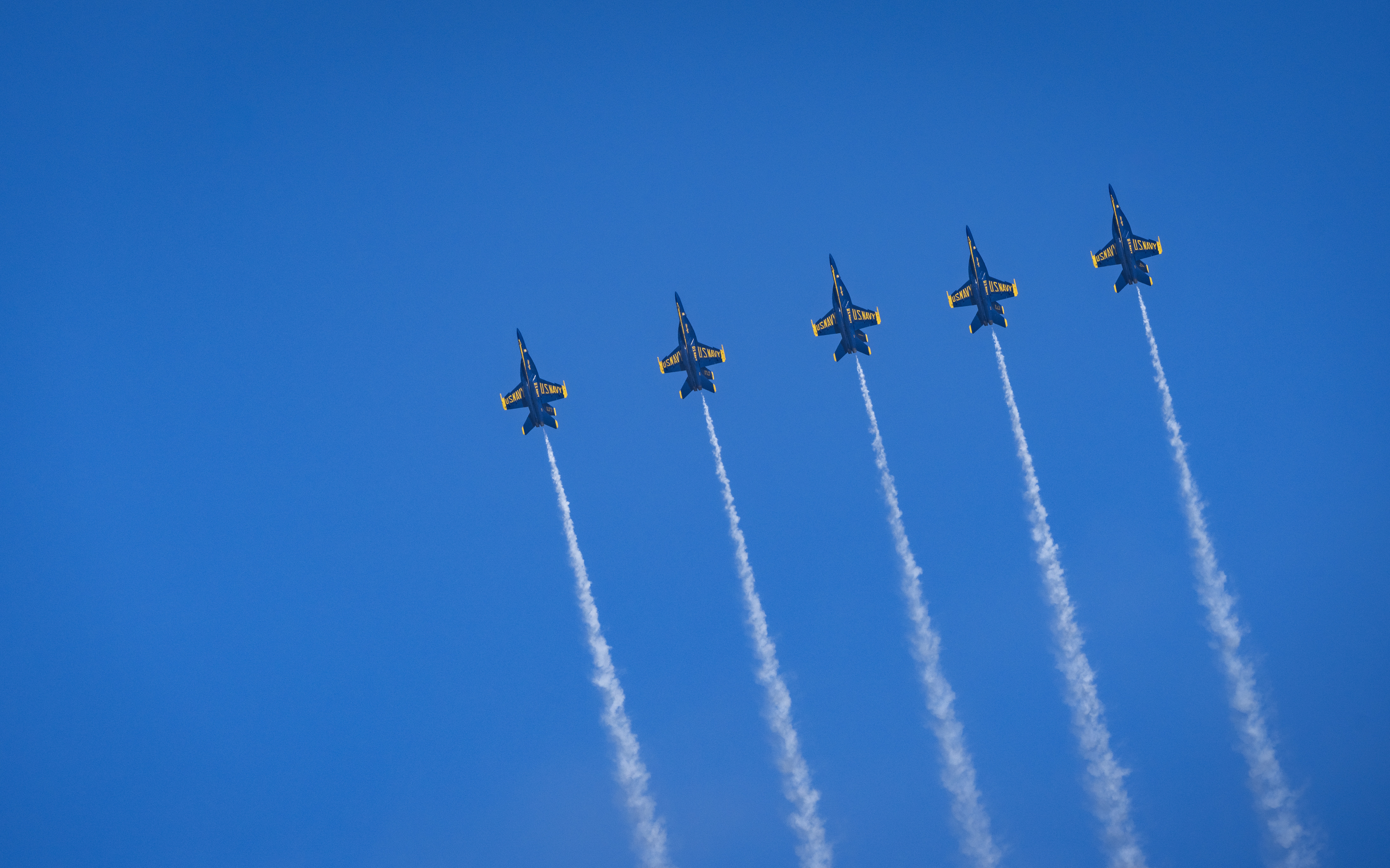 Blue Angels jets rise through the sky with several parallel smoke trails.