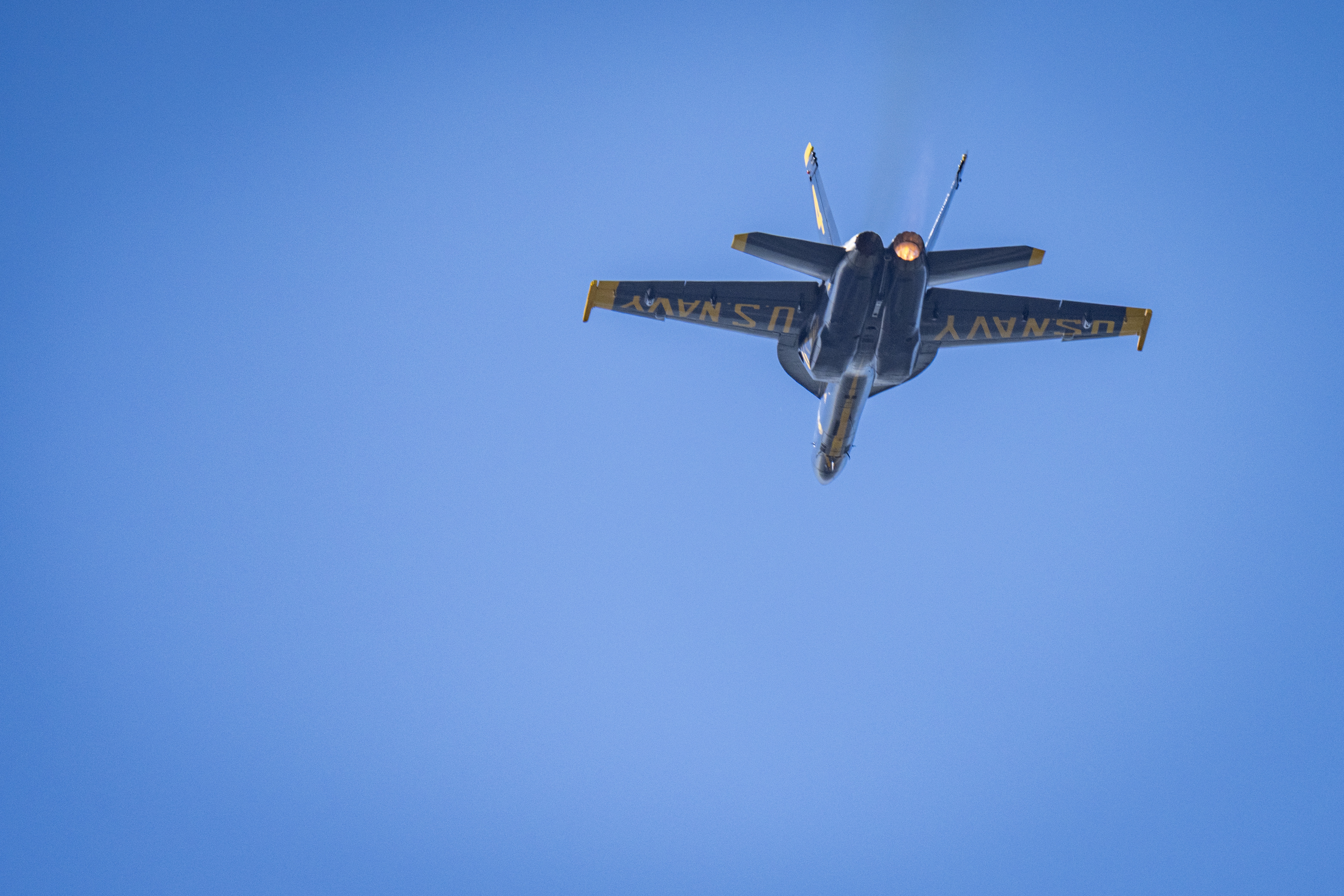 The underside of a Blue Angels jet shows U.S. Navy markings as it passes overhead.
