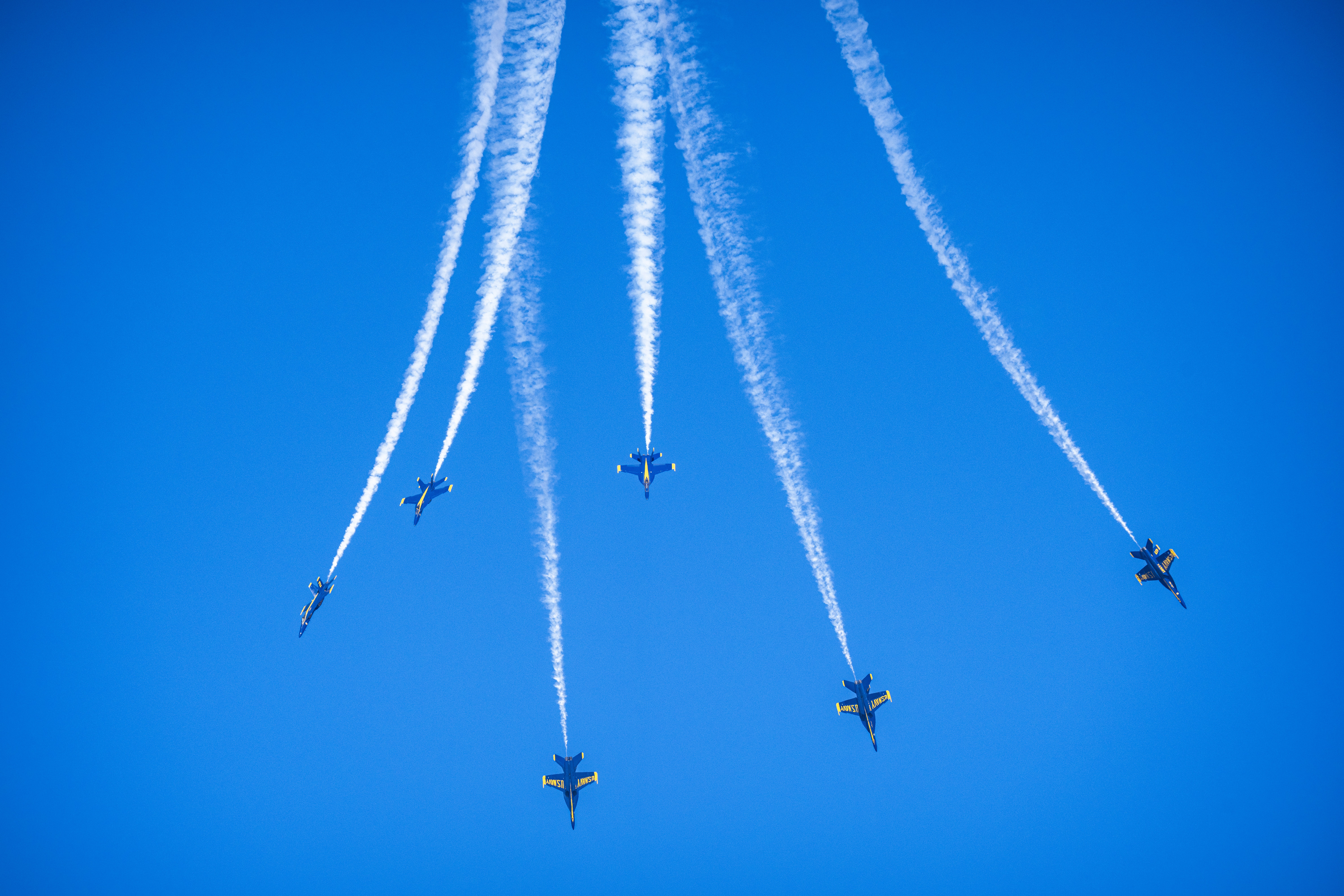 Blue Angels jets fly apart beneath white smoke trails that fan across the sky.