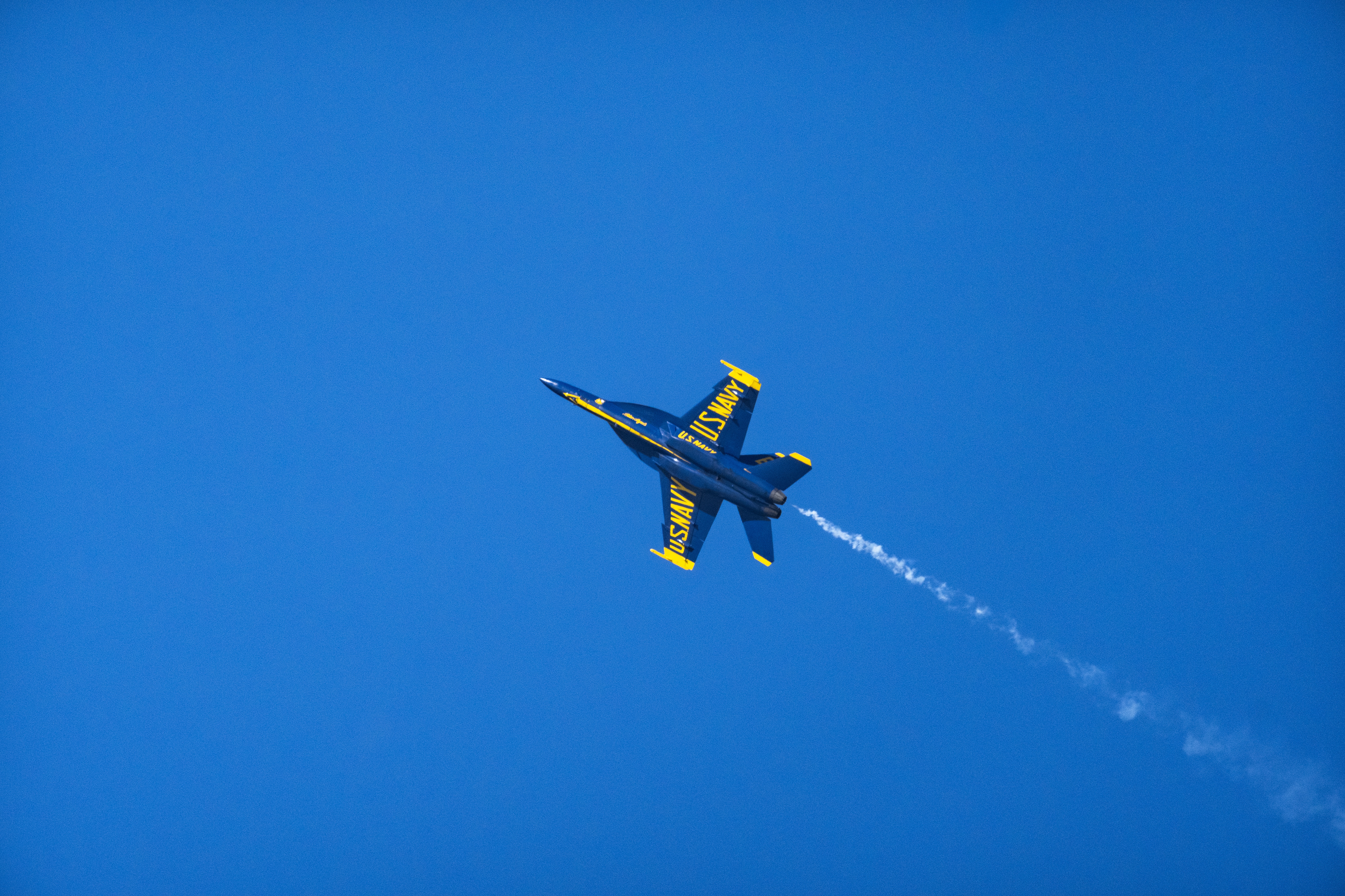 Blue Angels jet No. 5 banks through a turn with a white smoke trail behind it.