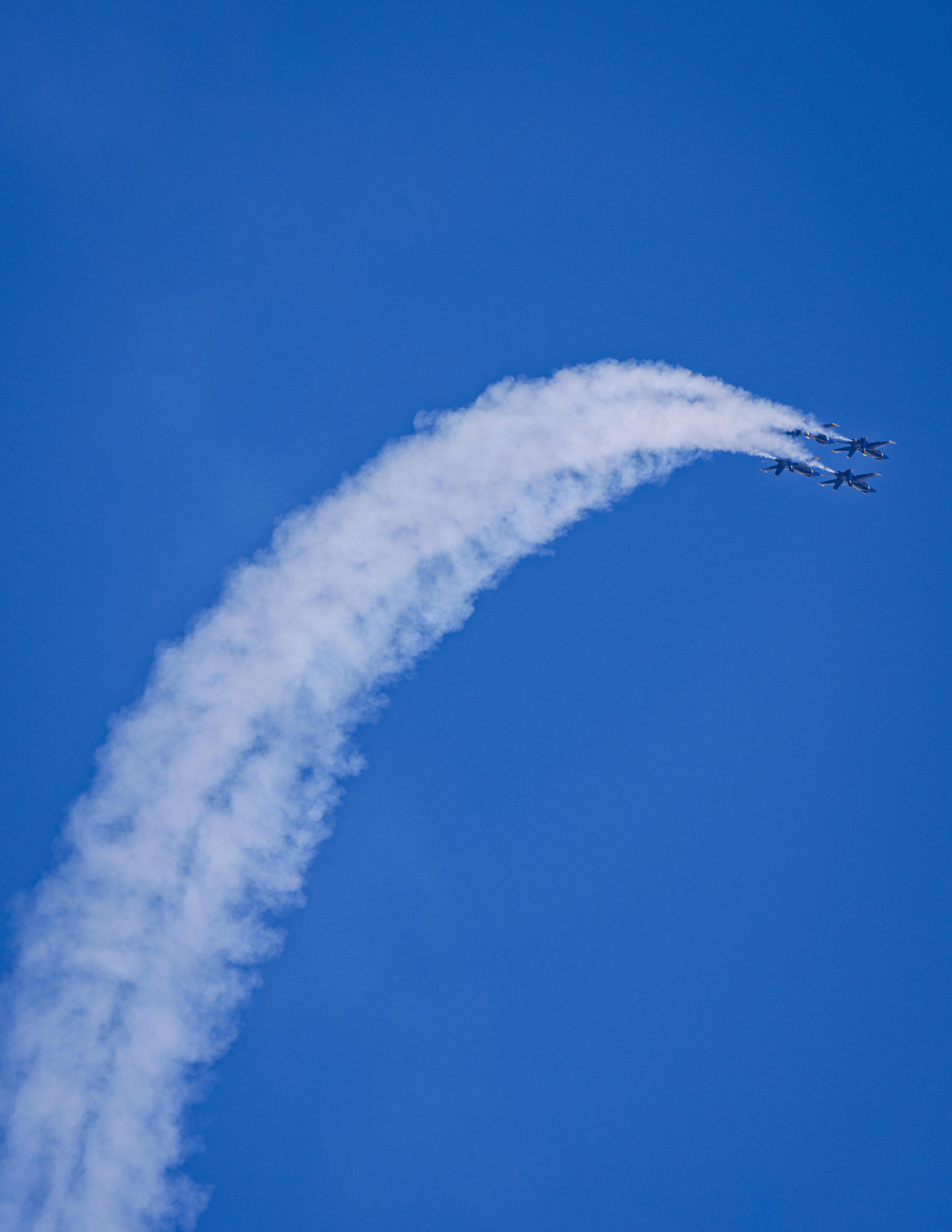 A Blue Angels jet banks through a curved smoke trail.