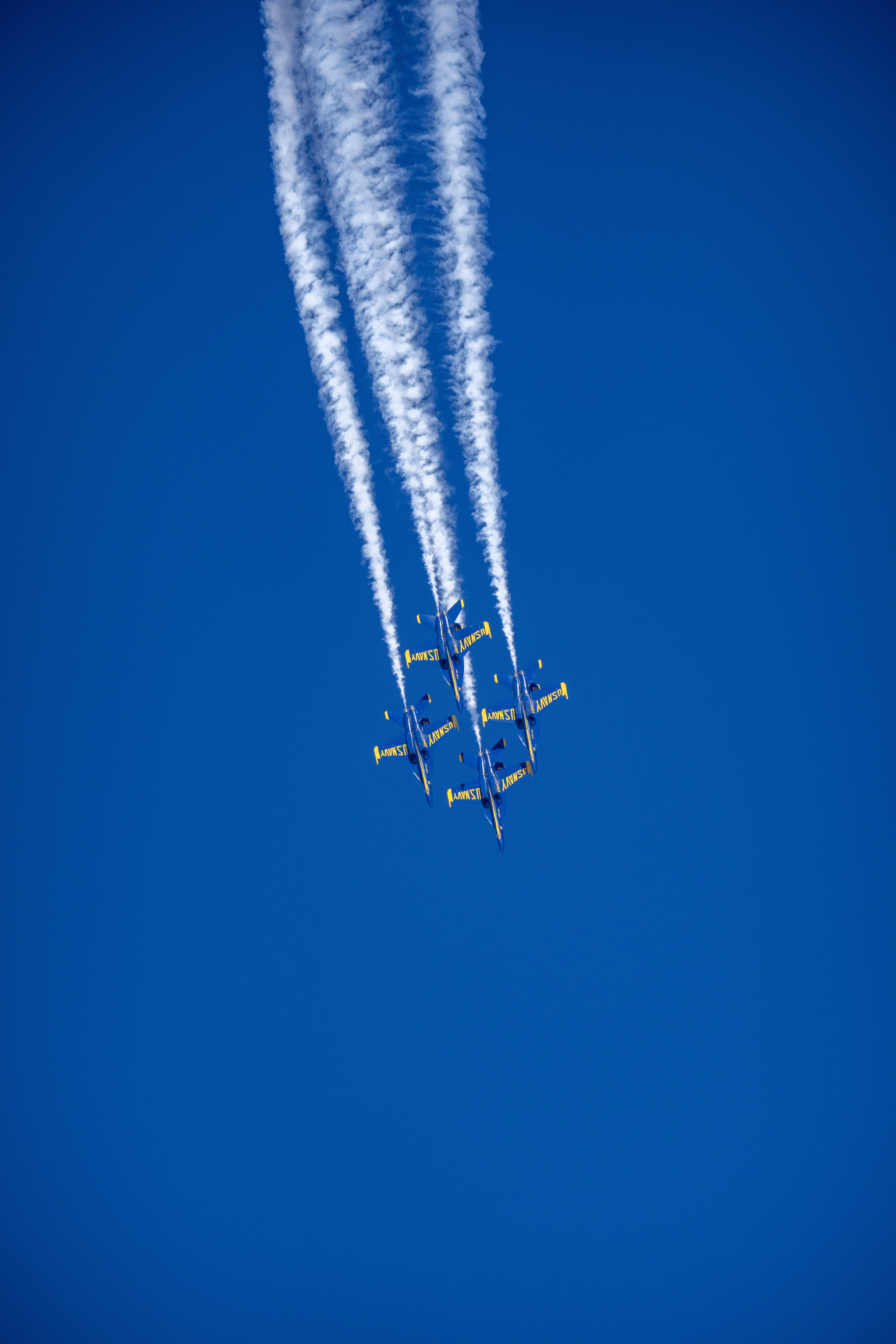 Blue Angels jets pass beneath several long parallel smoke trails.