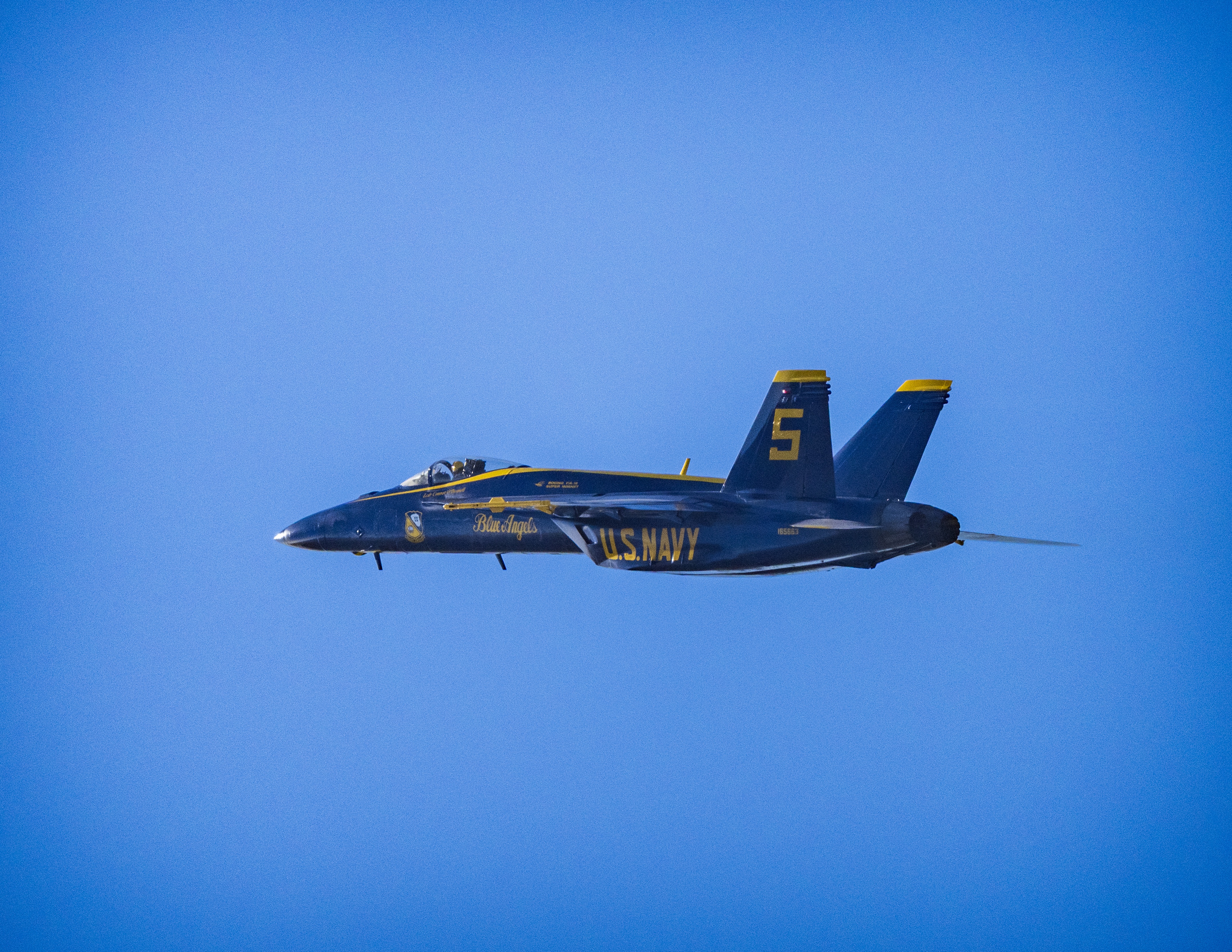 Blue Angels jet No. 5 crosses a clear blue sky in profile.