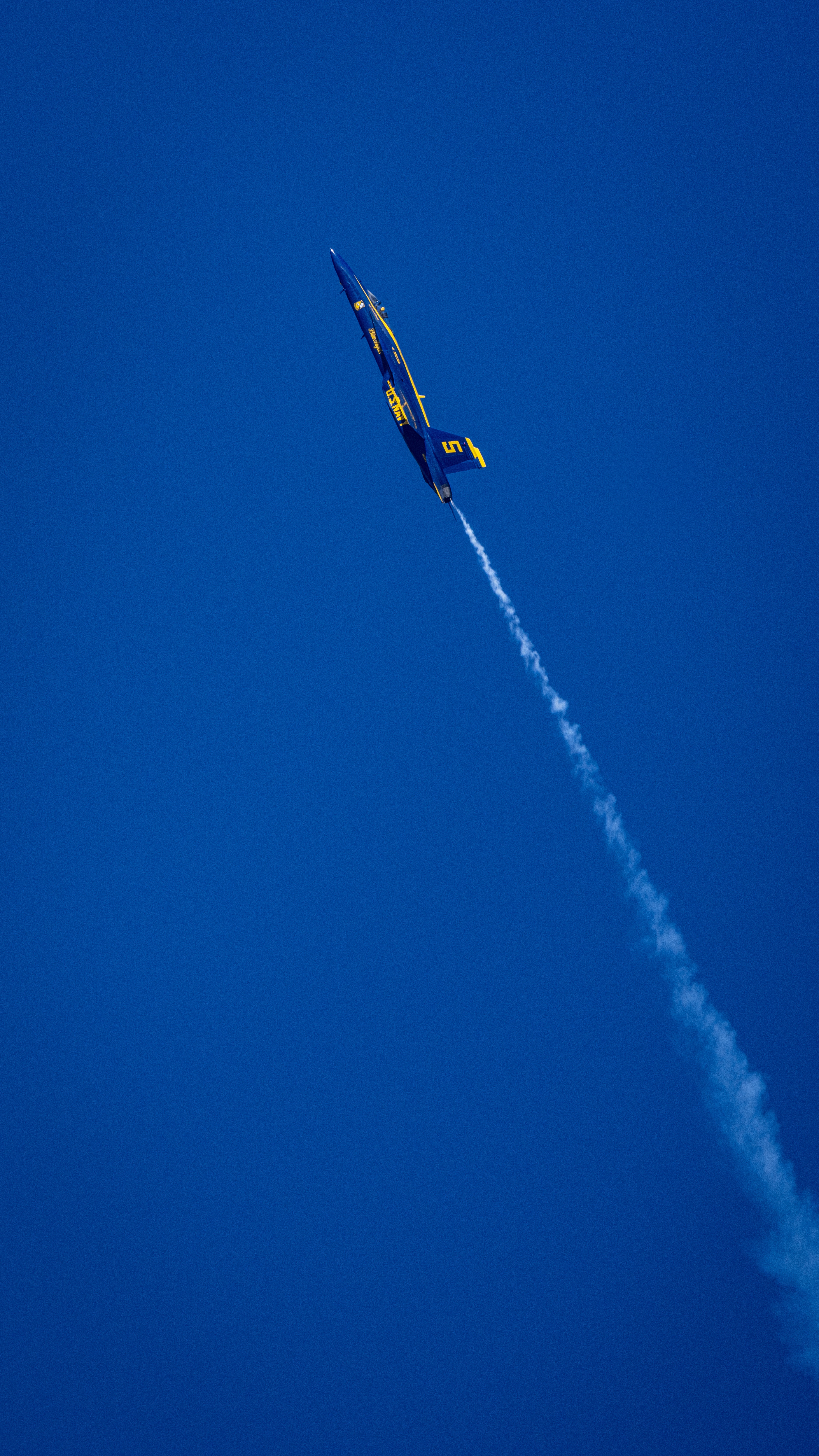 A Blue Angels jet appears along a long vertical smoke trail.