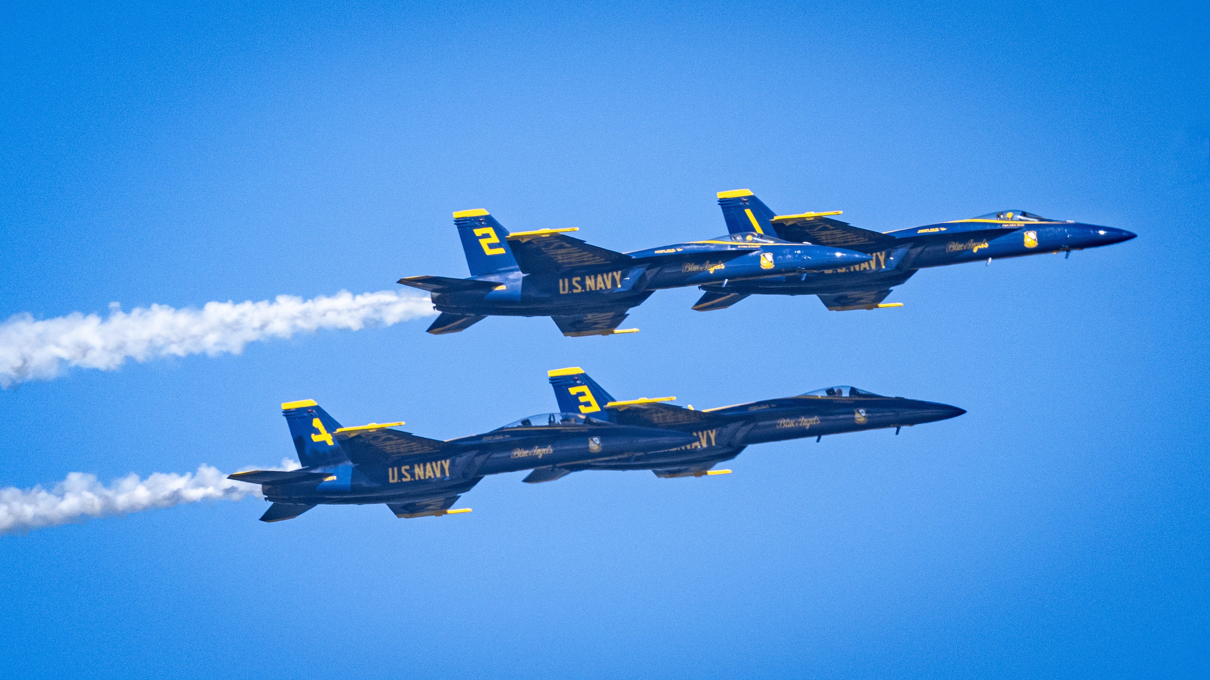 Blue Angels jets fly across the sky with parallel smoke trails.