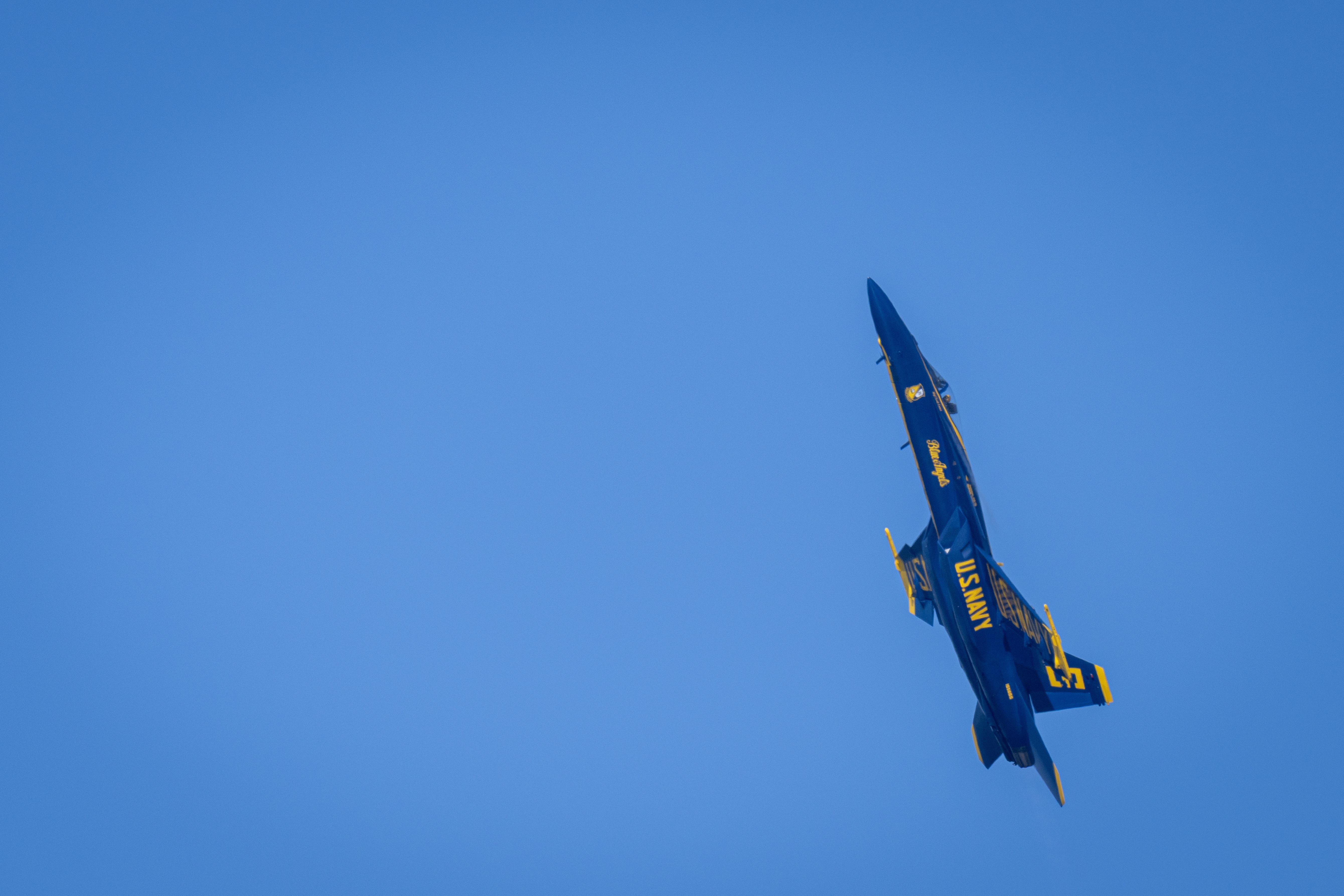 A Blue Angels jet banks steeply against the blue sky.
