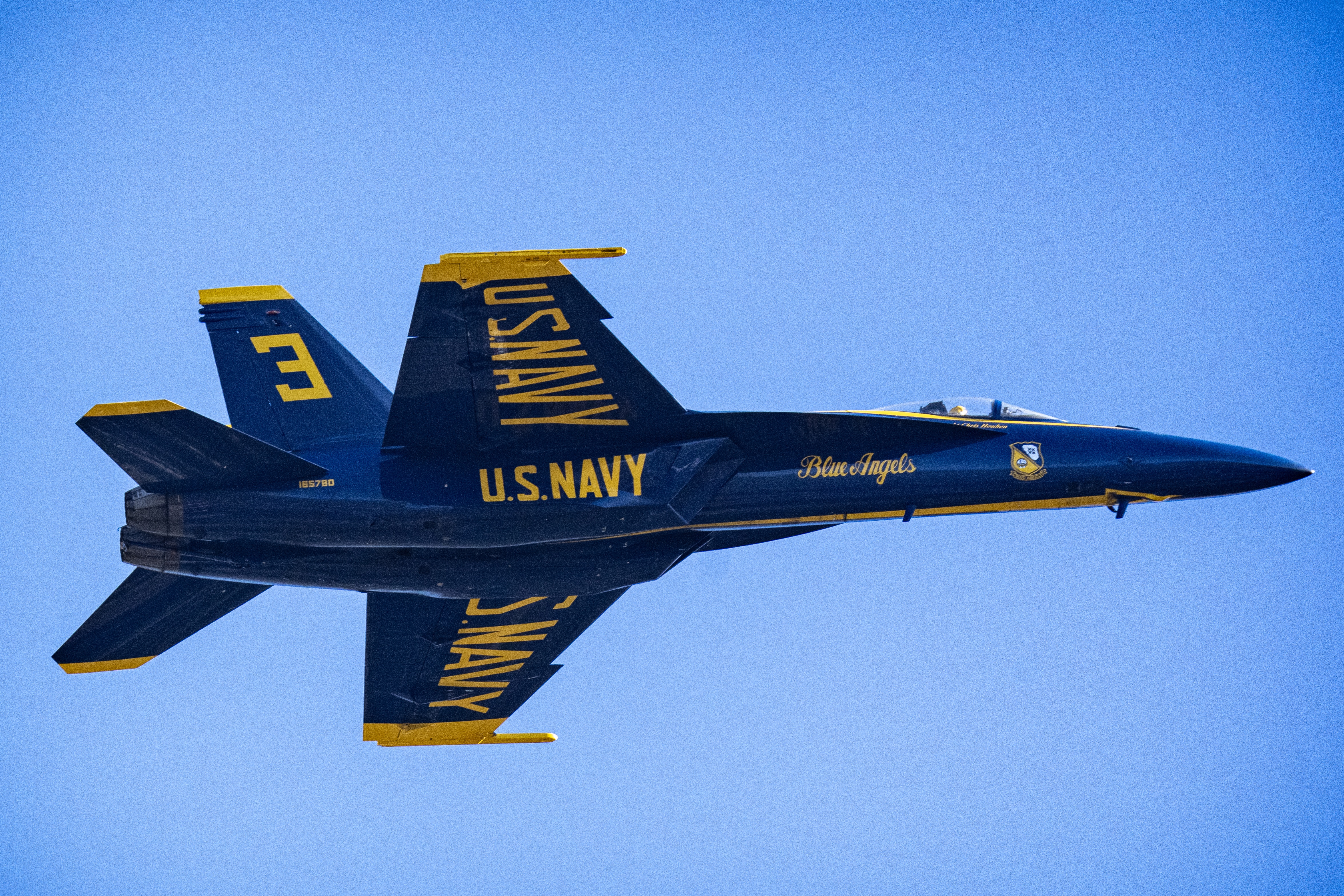 Blue Angels jet No. 3 flies in profile against a clear blue sky.