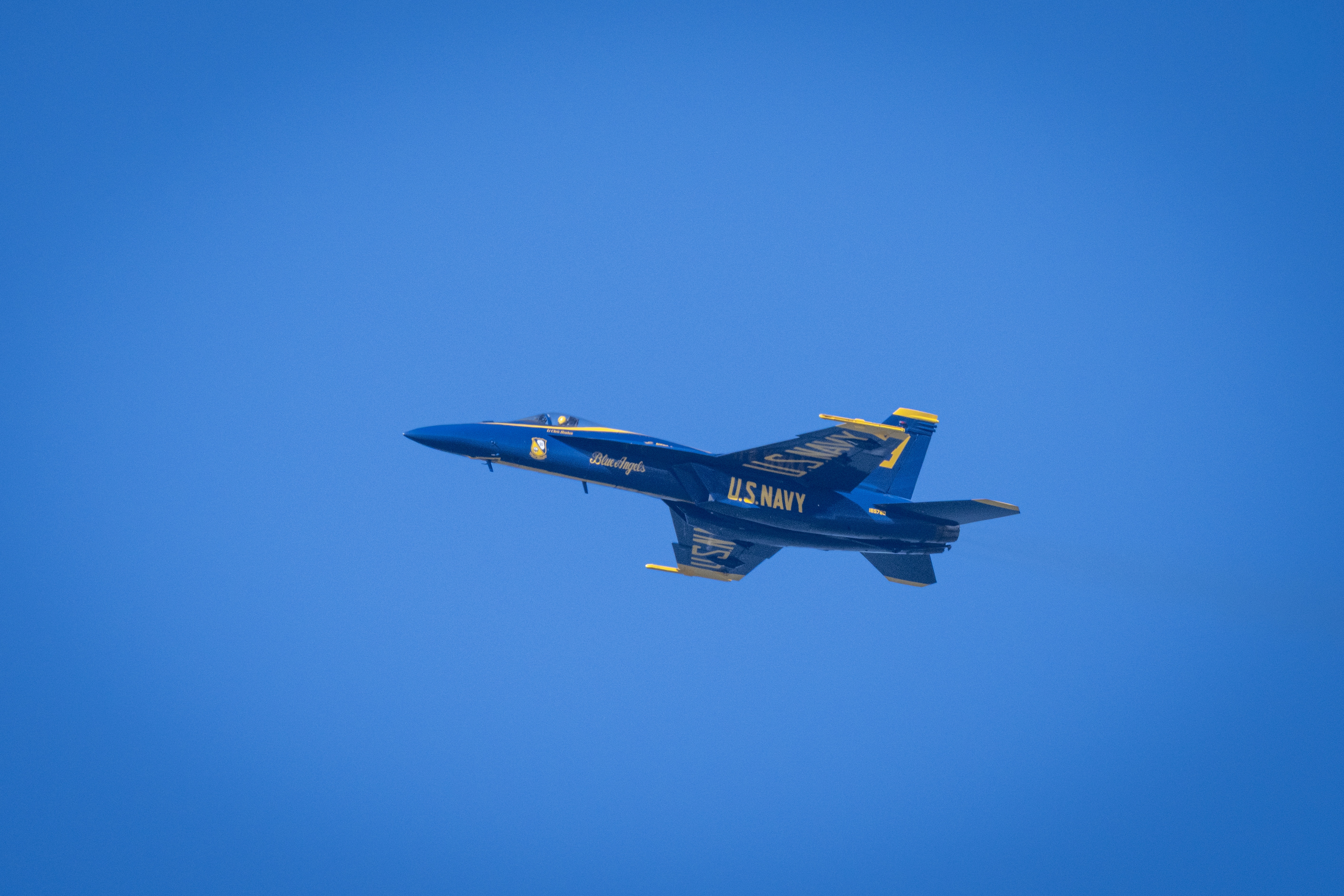 A Blue Angels jet flies in side profile against an open blue sky.