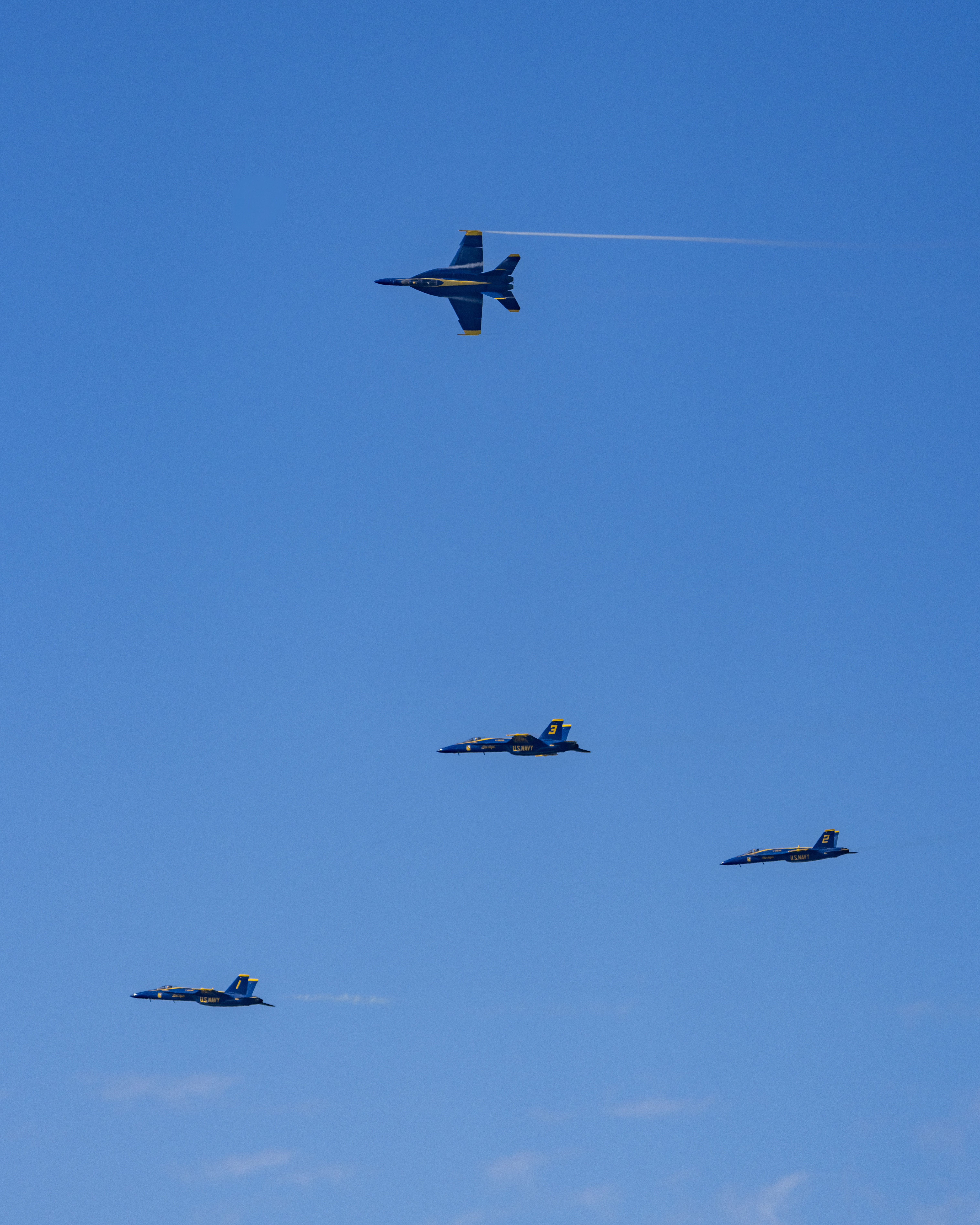 Blue Angels jets are spaced across a broad expanse of blue sky.