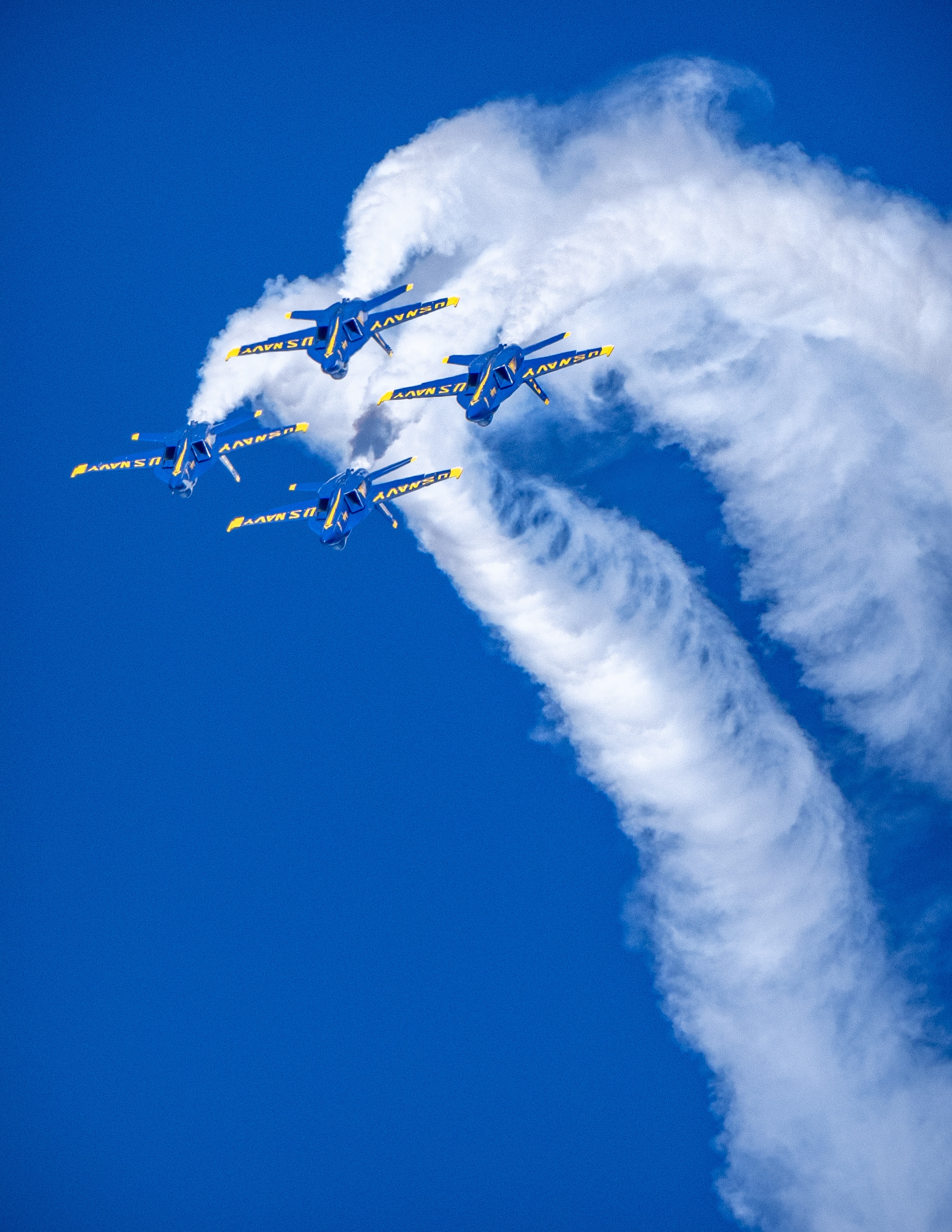 Blue Angels jets fly within a broad curved arc of white smoke.