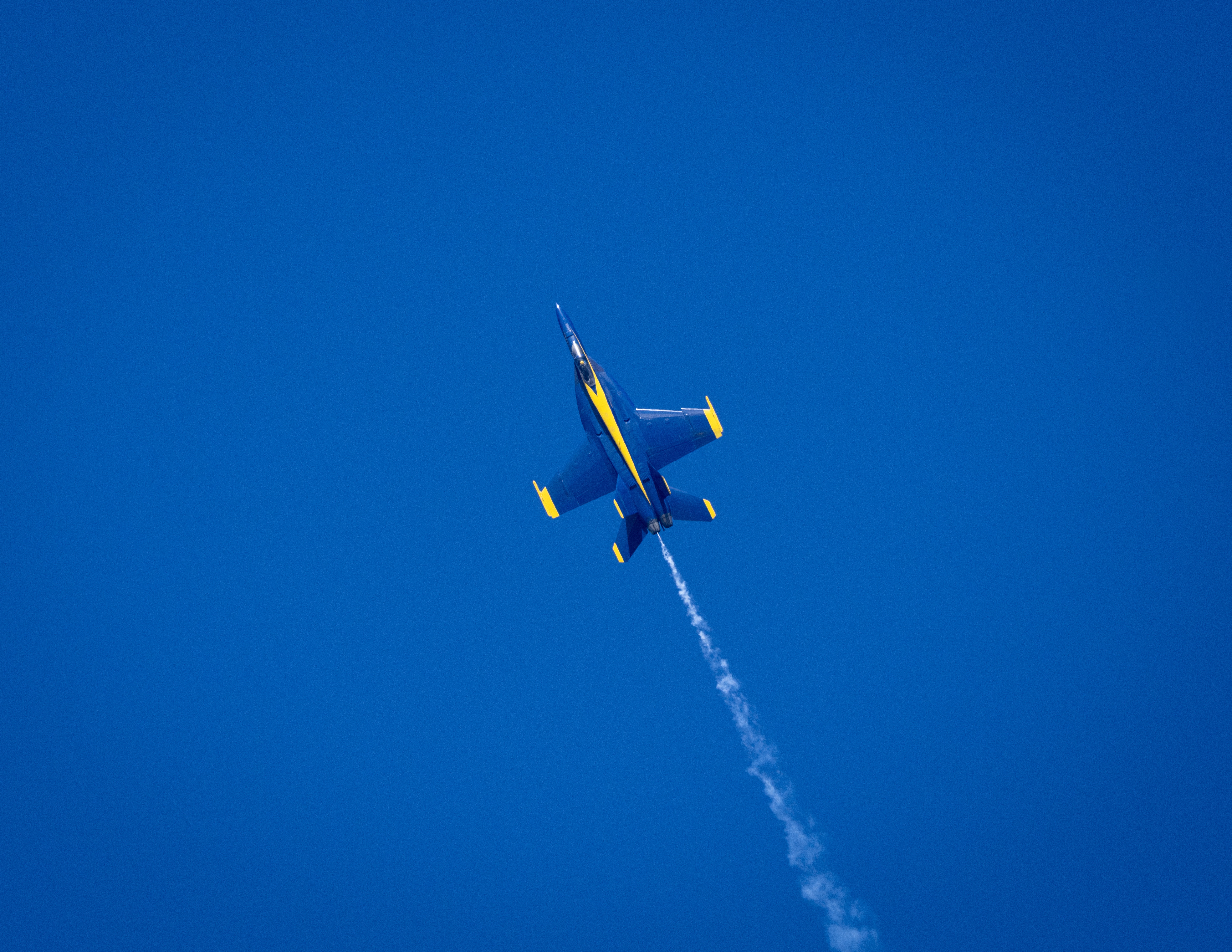 A Blue Angels jet banks upward through blue sky.
