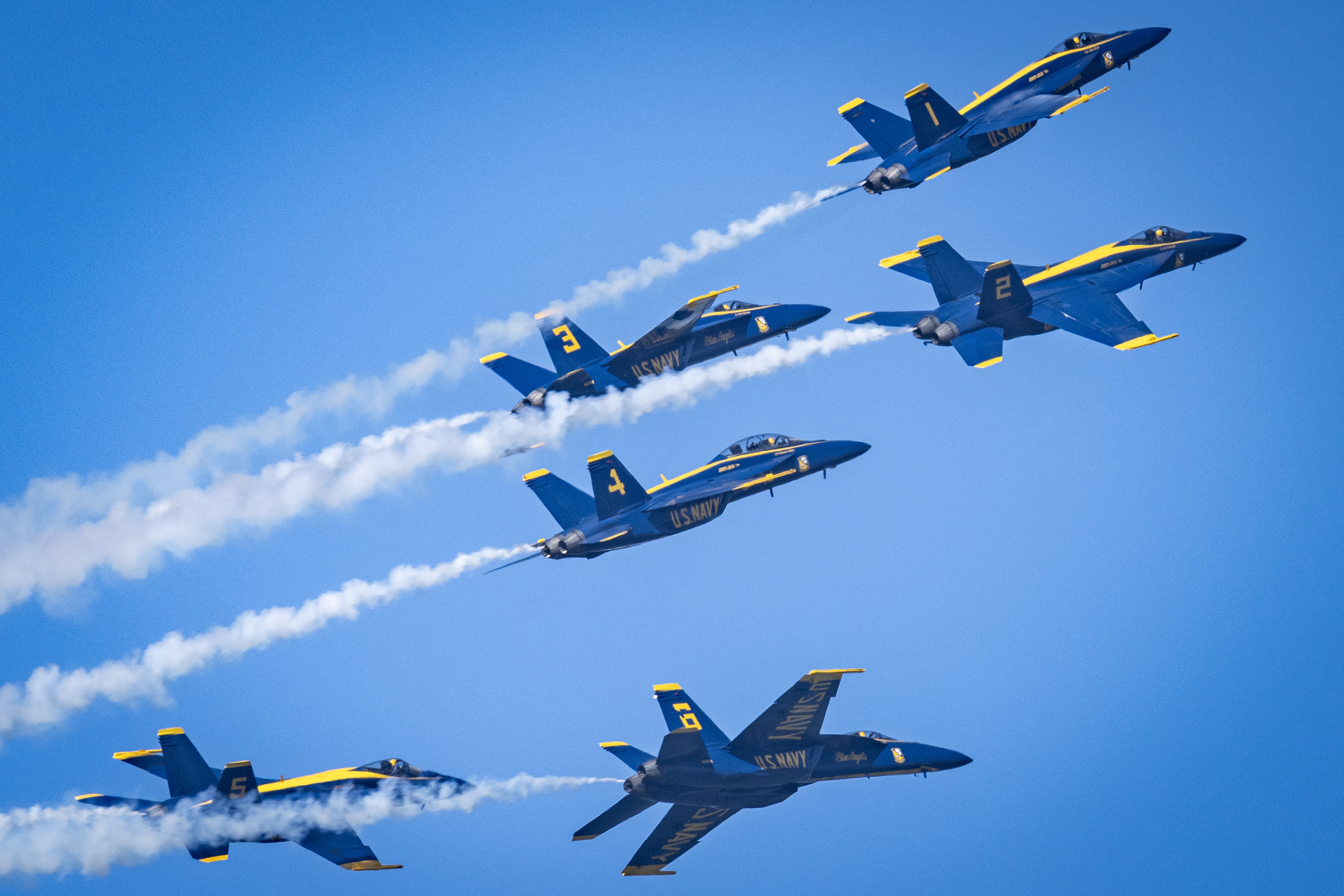 Blue Angels jets cross through the sky with intersecting smoke trails.
