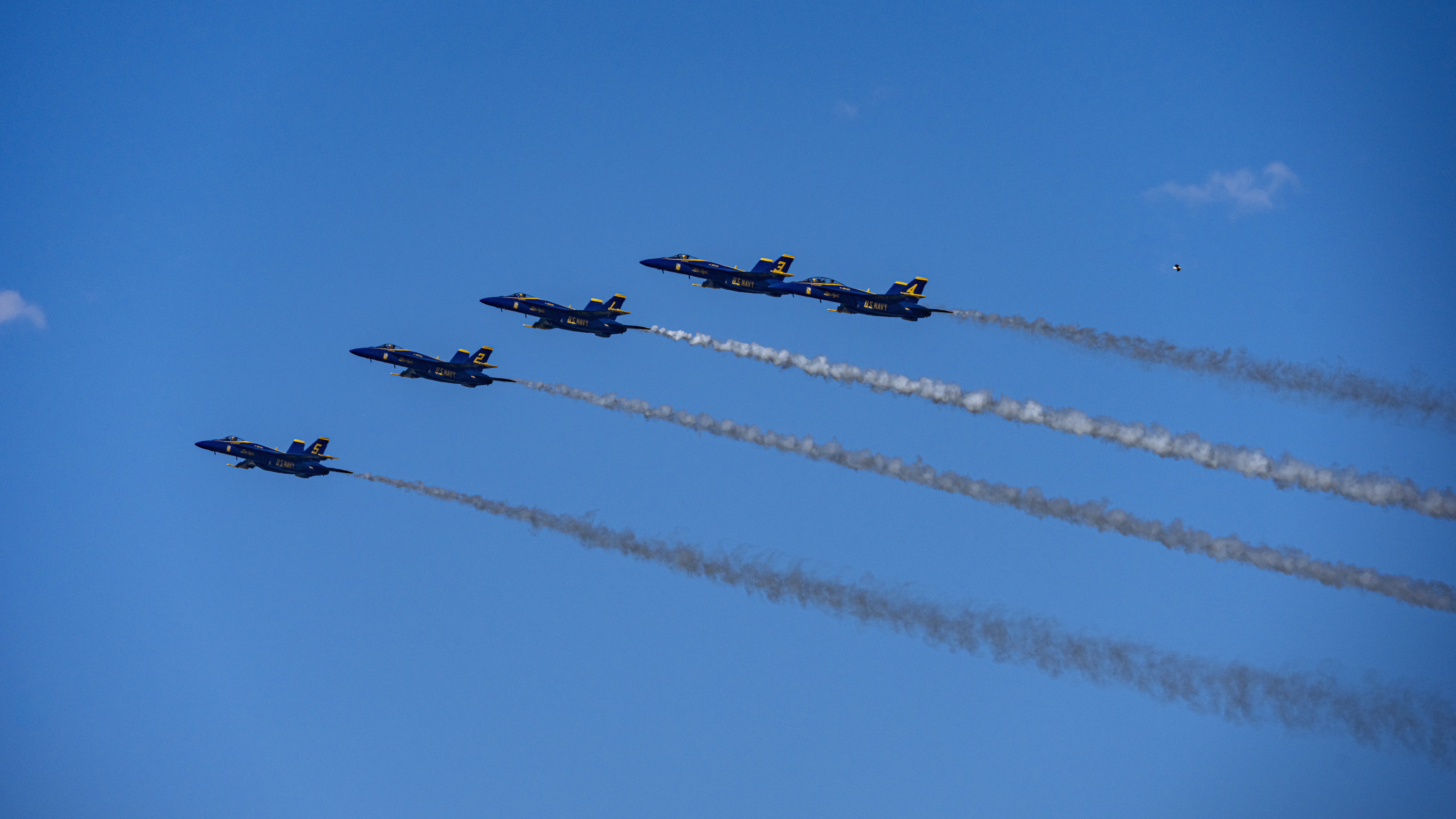 Blue Angels jets cross the frame beneath parallel white smoke trails.