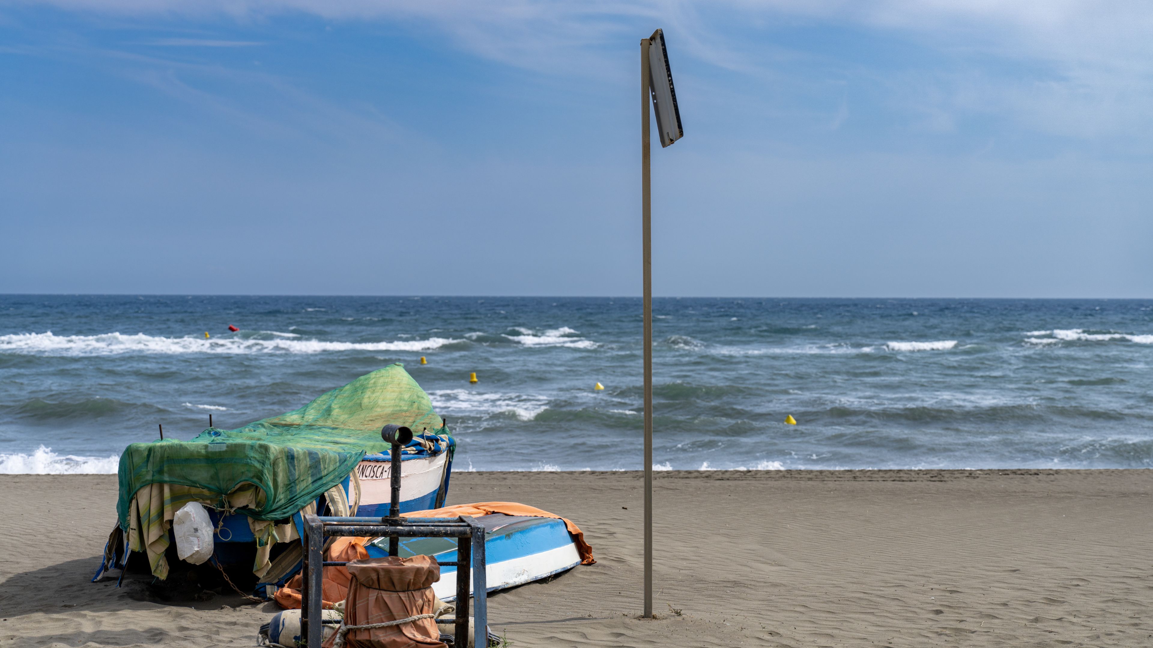Two boats are shown on the sandy beach, with the ocean waves and a signpost in the background.