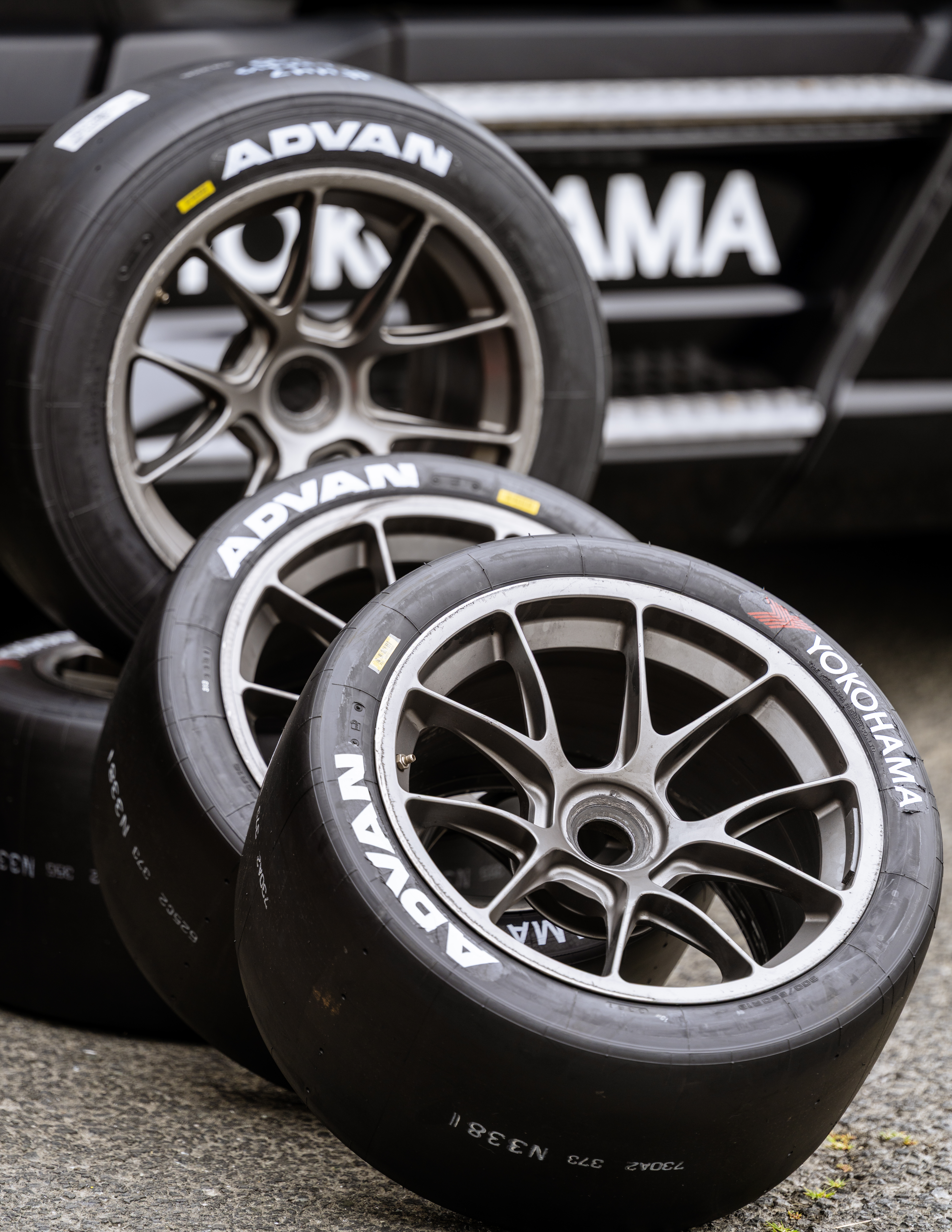 Three mounted ADVAN racing tires lean against one another beside a black Yokohama paddock barrier.