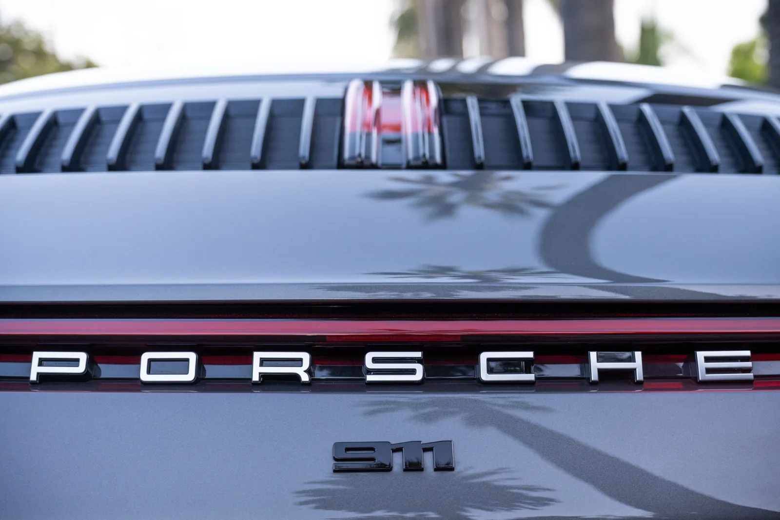 Close-up of a Porsche rear showing the PORSCHE and 911 Carrera S badges, grille, red trim, and palm tree reflections.