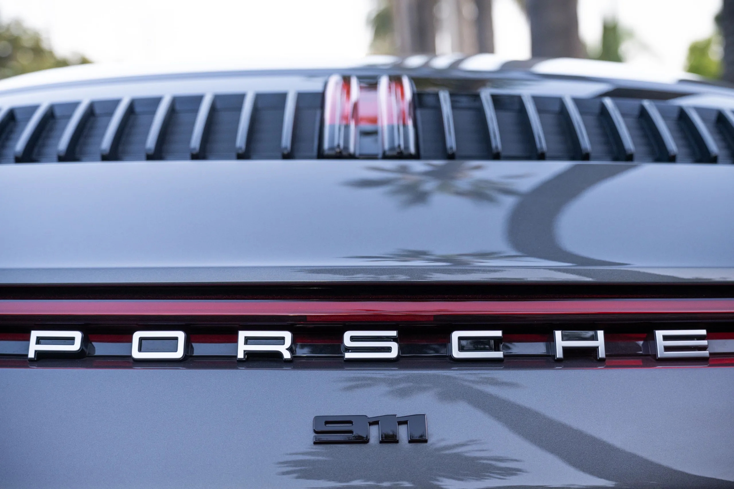 Close-up of a Porsche rear showing the PORSCHE and 911 Carrera S badges, grille, red trim, and palm tree reflections.