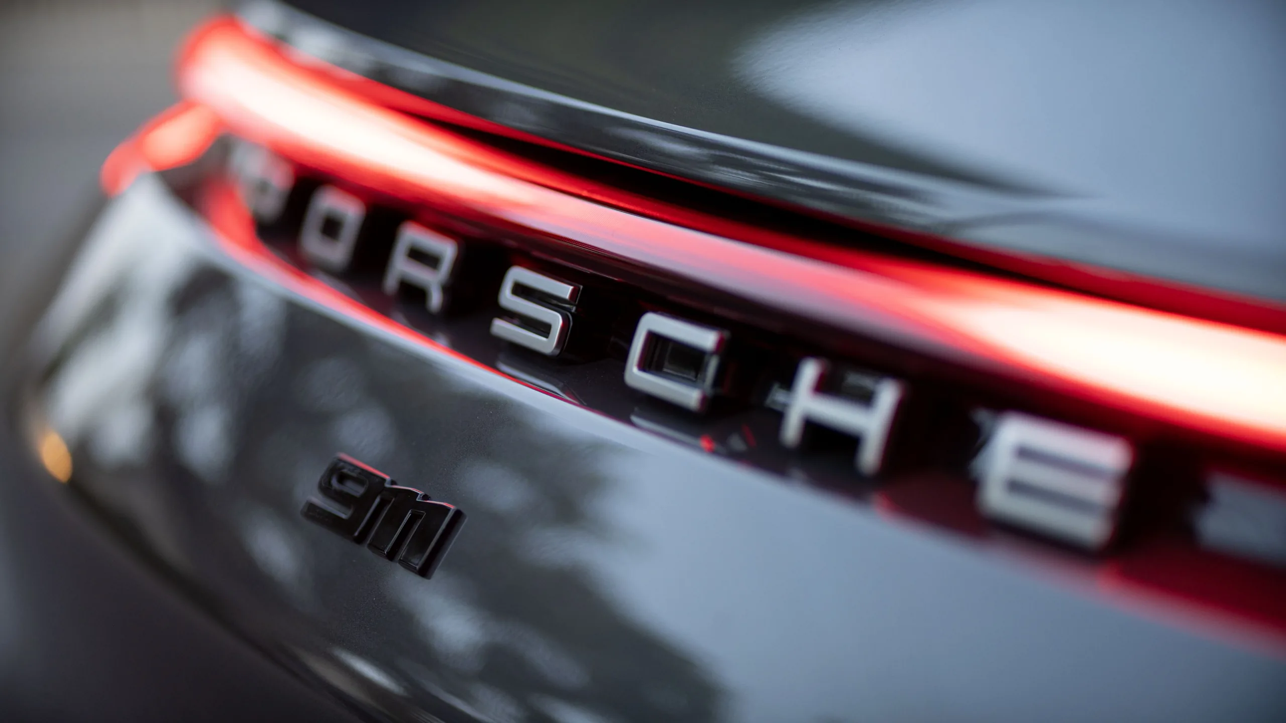 Shallow-focus close-up of Porsche lettering and a 911 S badge beneath a bright red rear light strip.