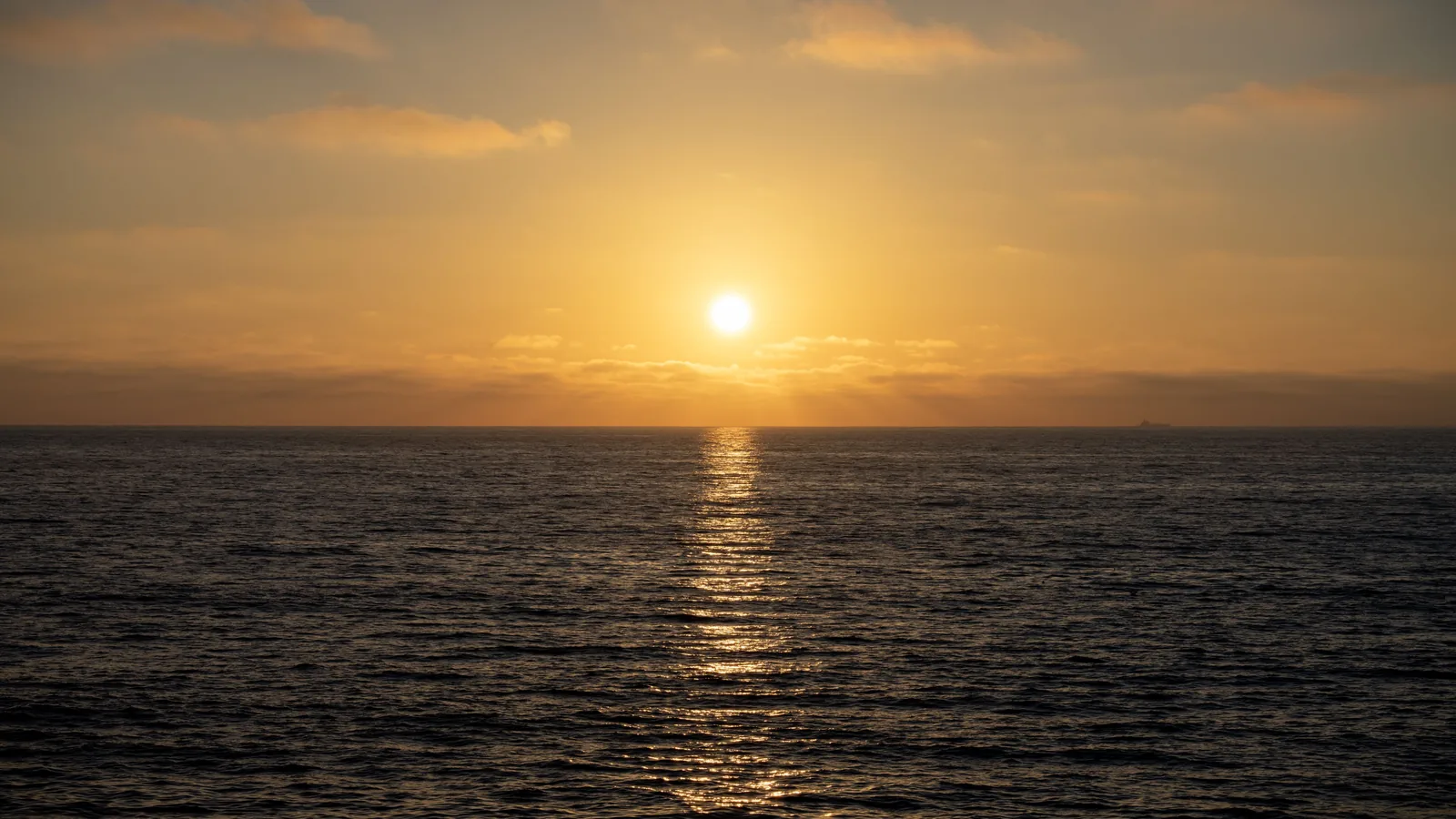 The sun sits above the ocean horizon, casting a narrow golden reflection across dark rippling water.