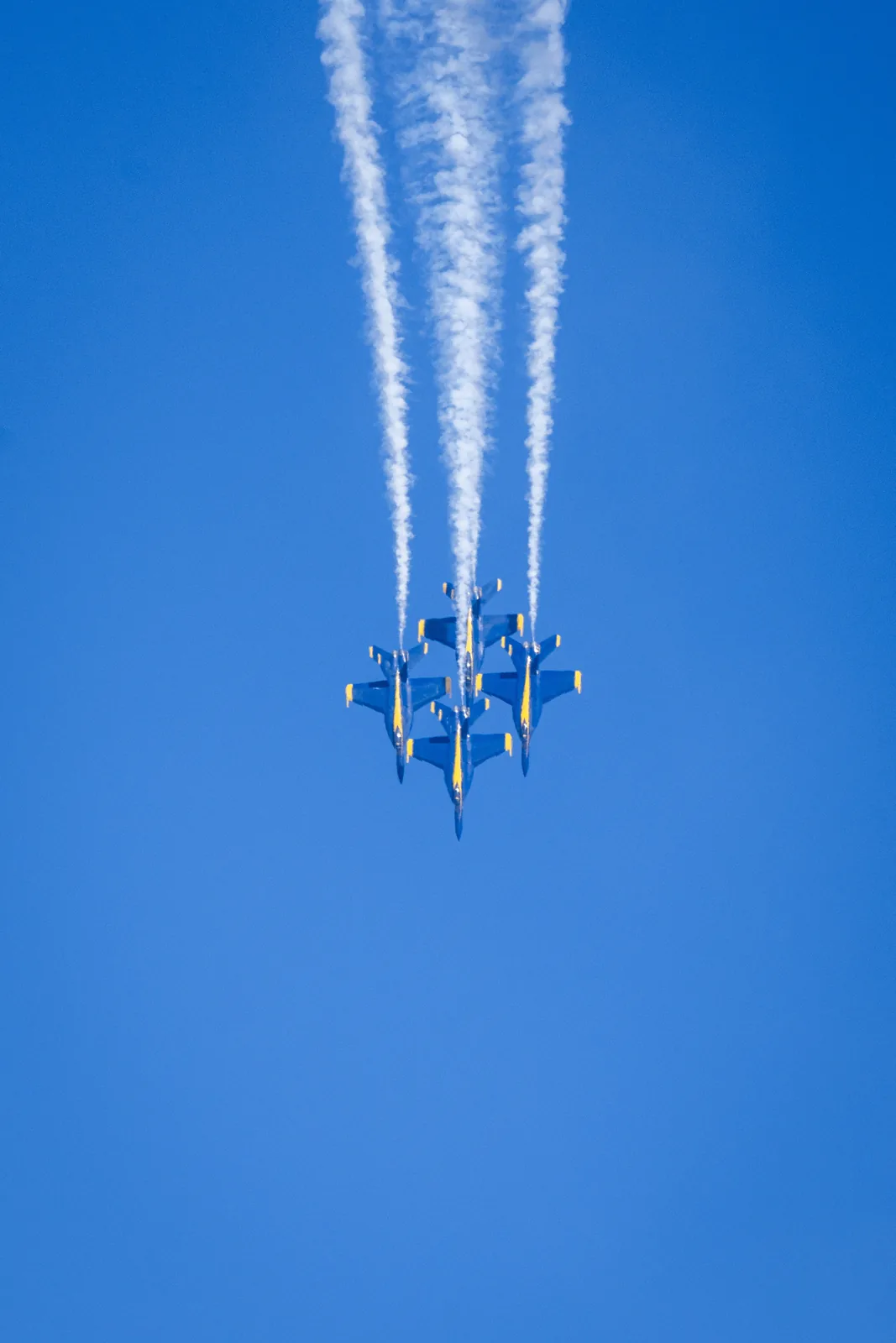 Blue Angels jets pass in formation amid tall white smoke trails.