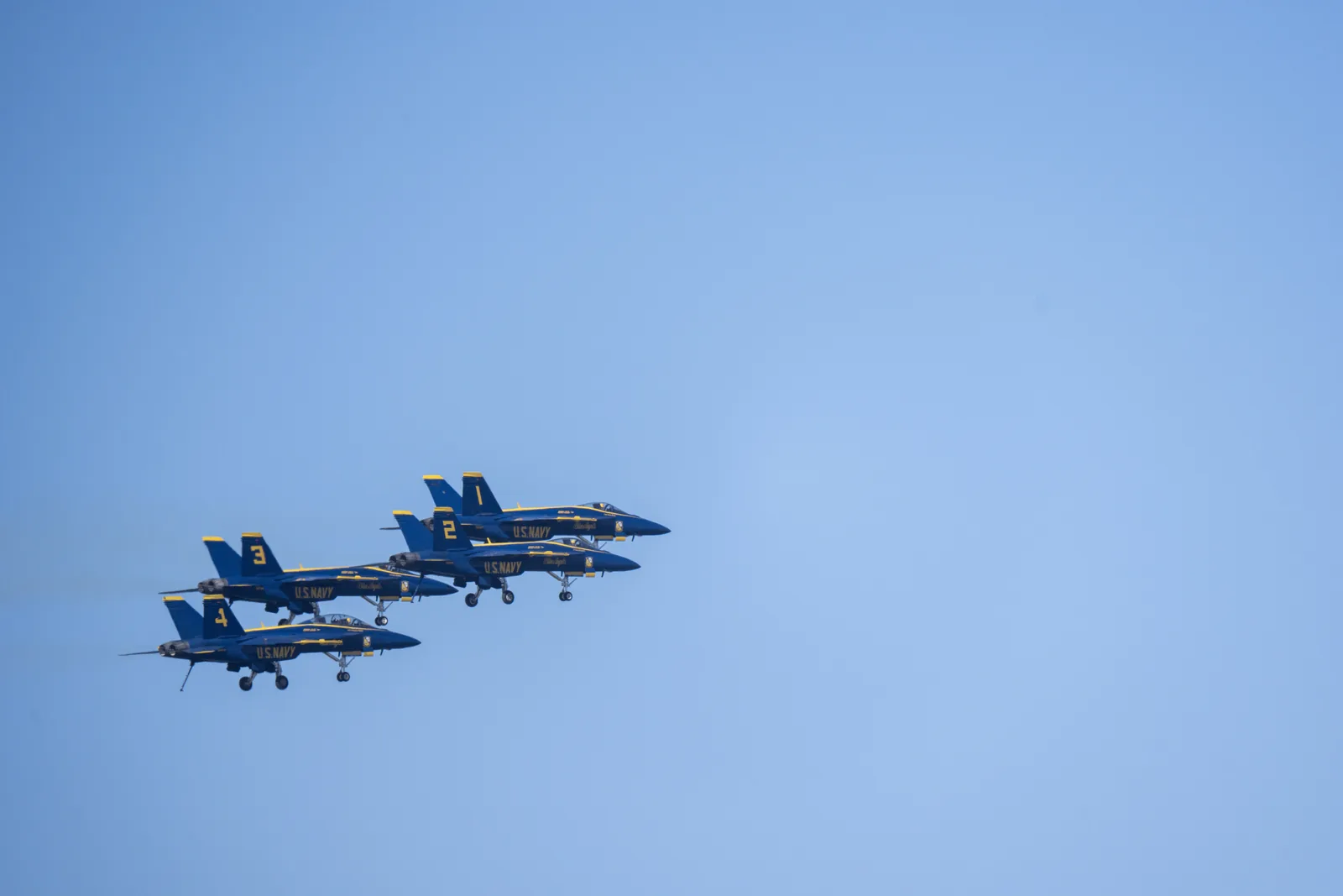 Blue Angels jets fly tightly together against a clear blue sky.
