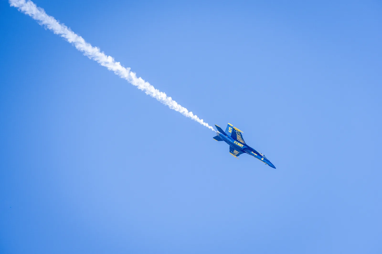 A Blue Angels jet passes below crossing white smoke trails.