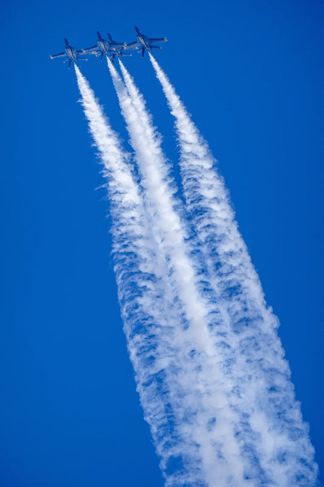 Four Blue Angels jets pass together with thick white smoke trails.