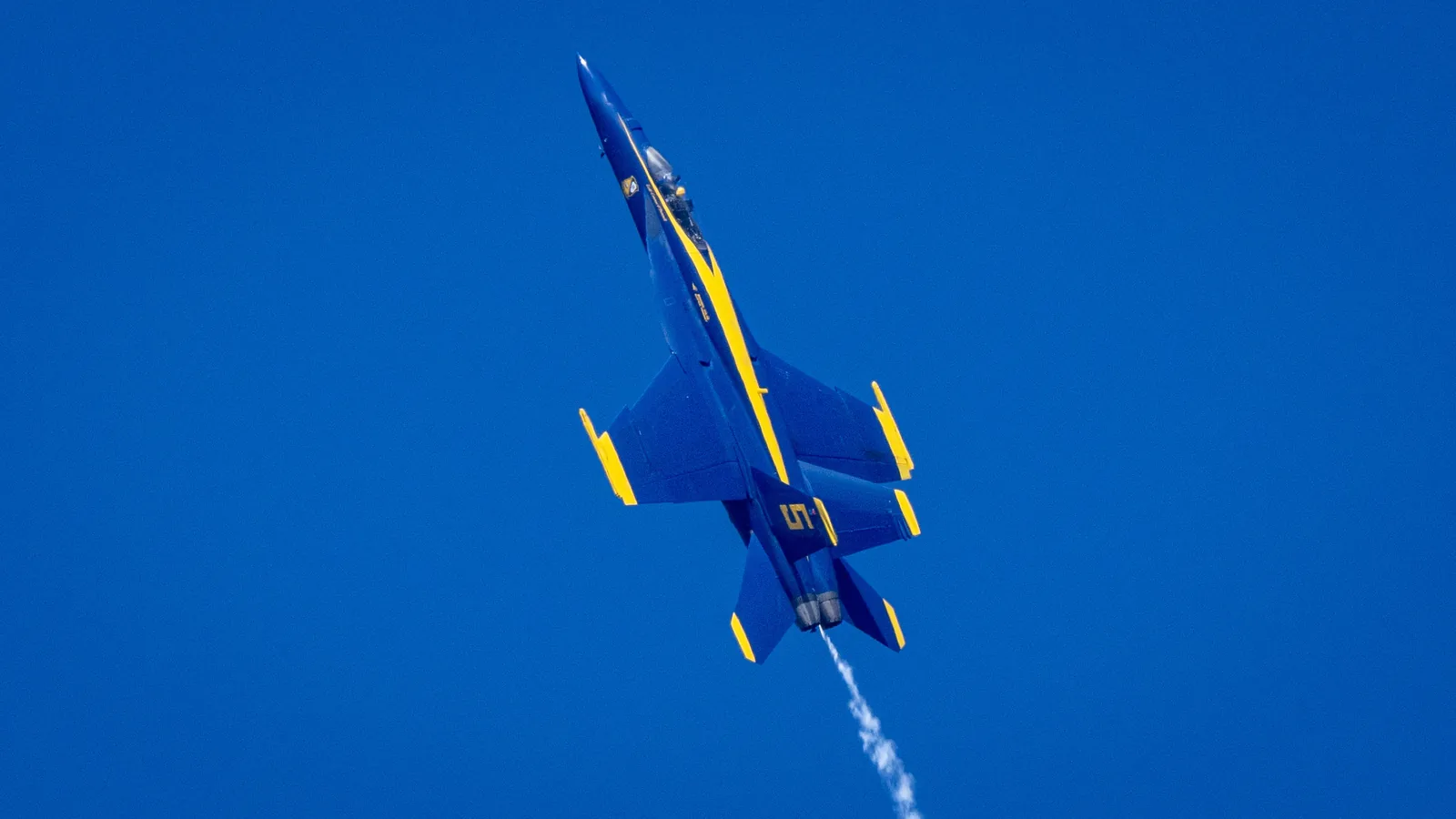 The underside of a Blue Angels jet passes against a clear sky.