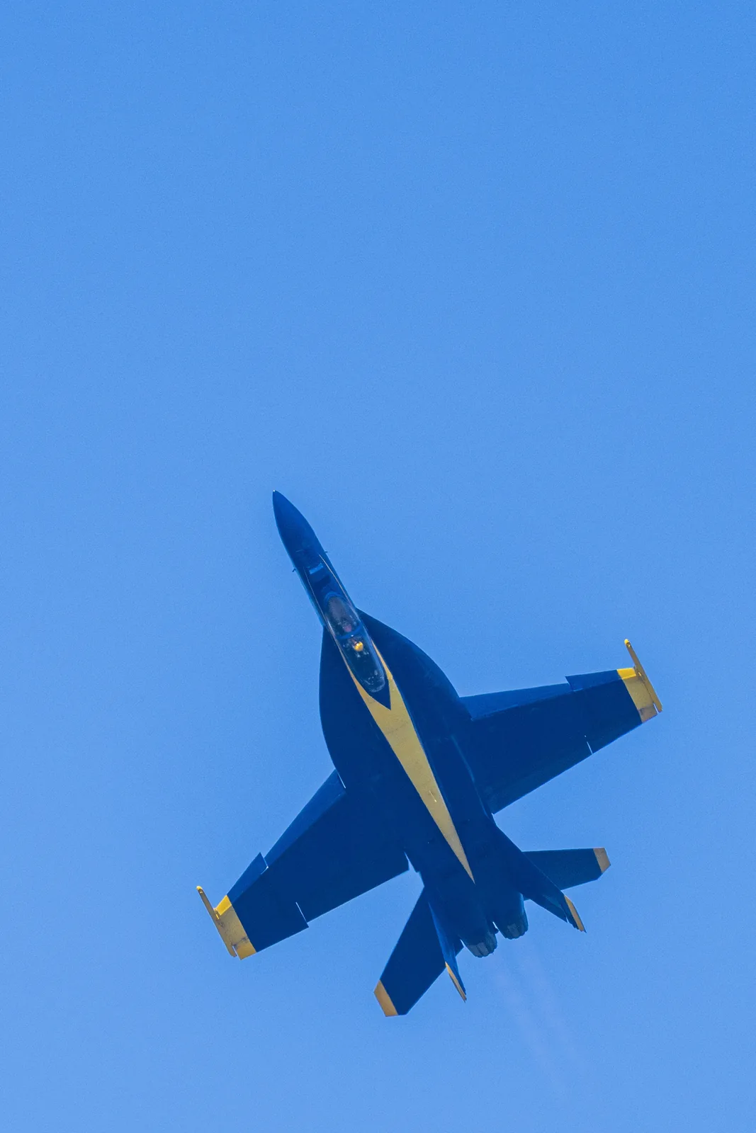 A close view of a Blue Angels jet's underside against blue sky.
