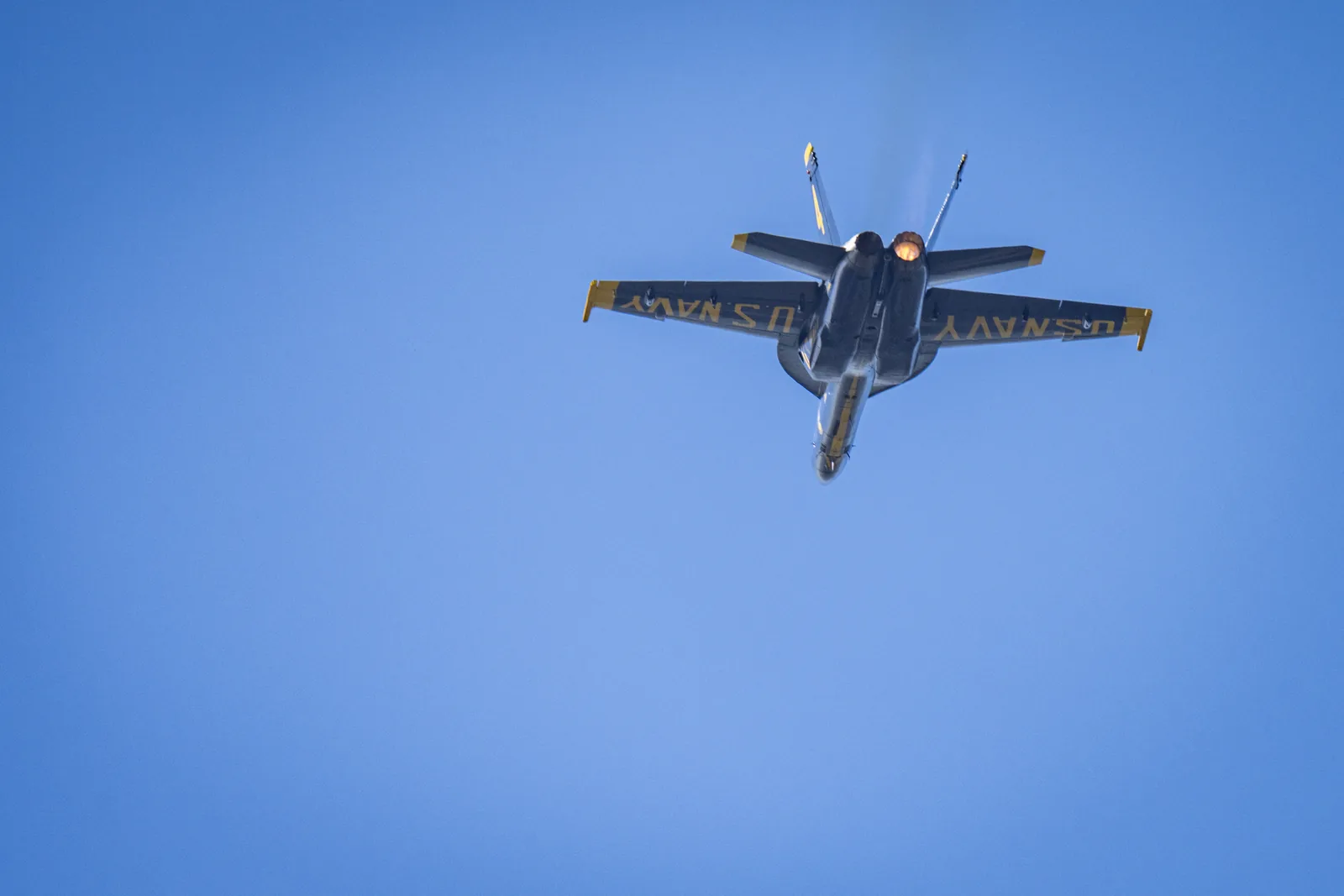 The underside of a Blue Angels jet shows U.S. Navy markings as it passes overhead.
