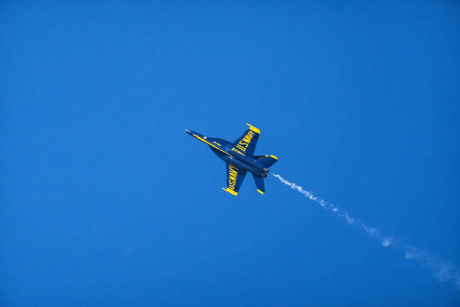 Blue Angels jet No. 5 banks through a turn with a white smoke trail behind it.