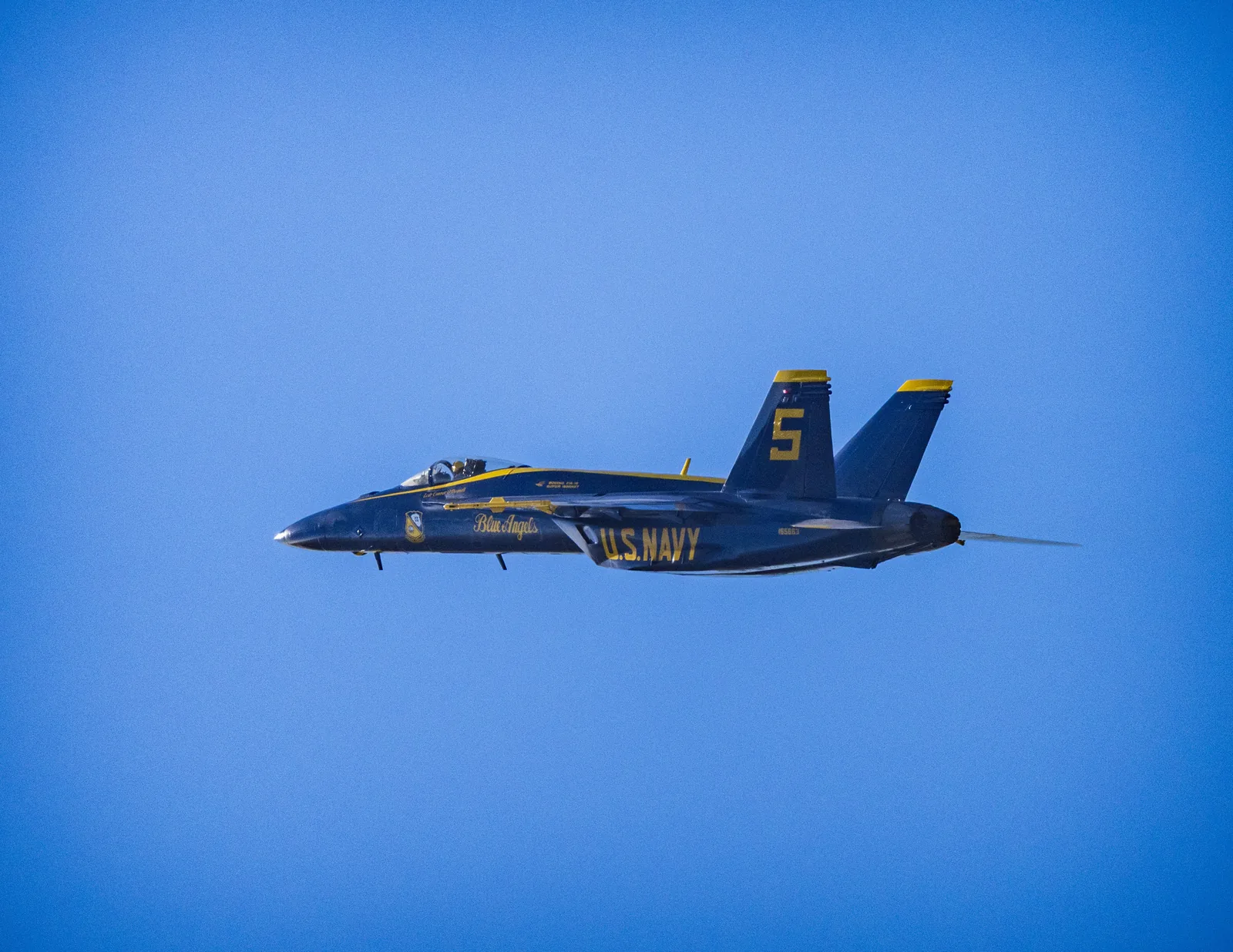 Blue Angels jet No. 5 crosses a clear blue sky in profile.