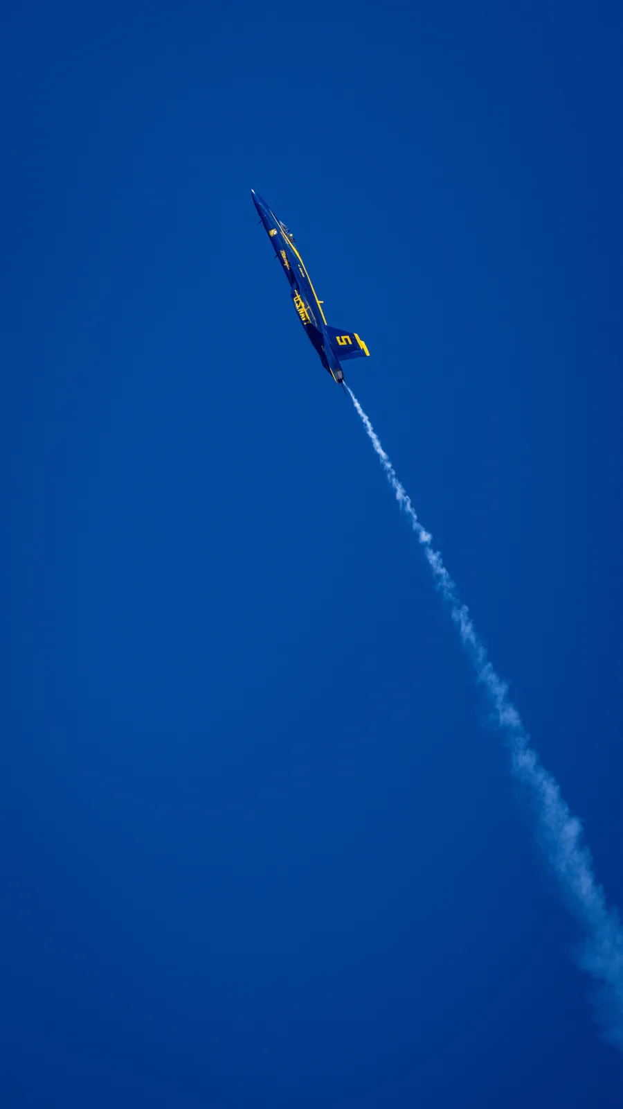 A Blue Angels jet appears along a long vertical smoke trail.