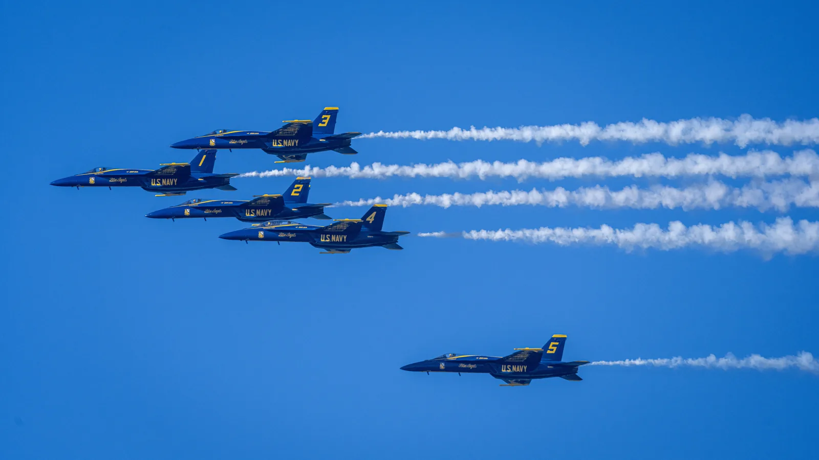 A Blue Angels jet trails a close group of aircraft in the sky.