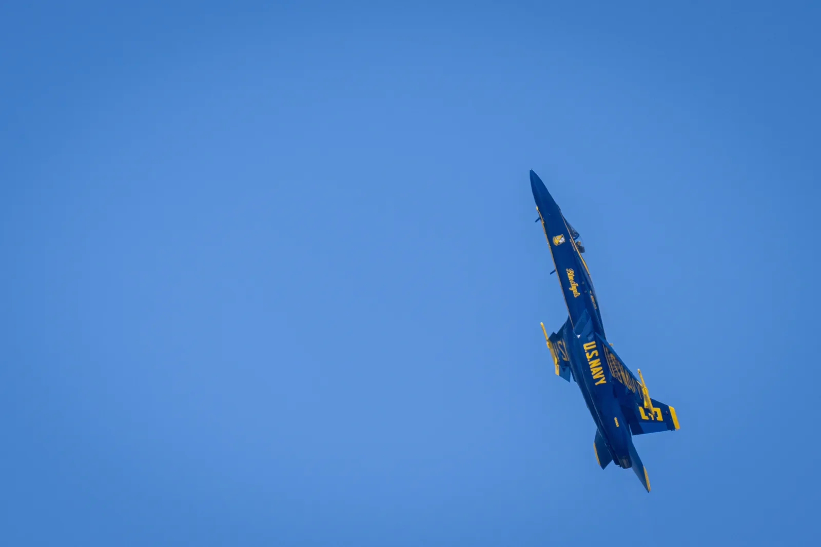 A Blue Angels jet banks steeply against the blue sky.