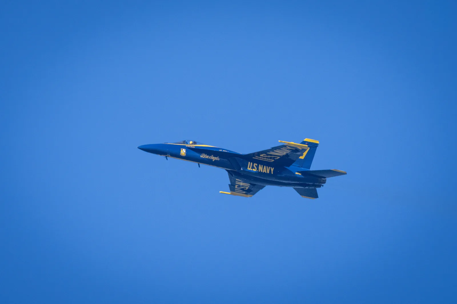 A Blue Angels jet flies in side profile against an open blue sky.