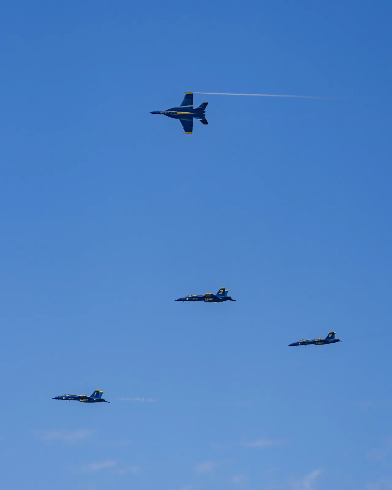 Blue Angels jets are spaced across a broad expanse of blue sky.