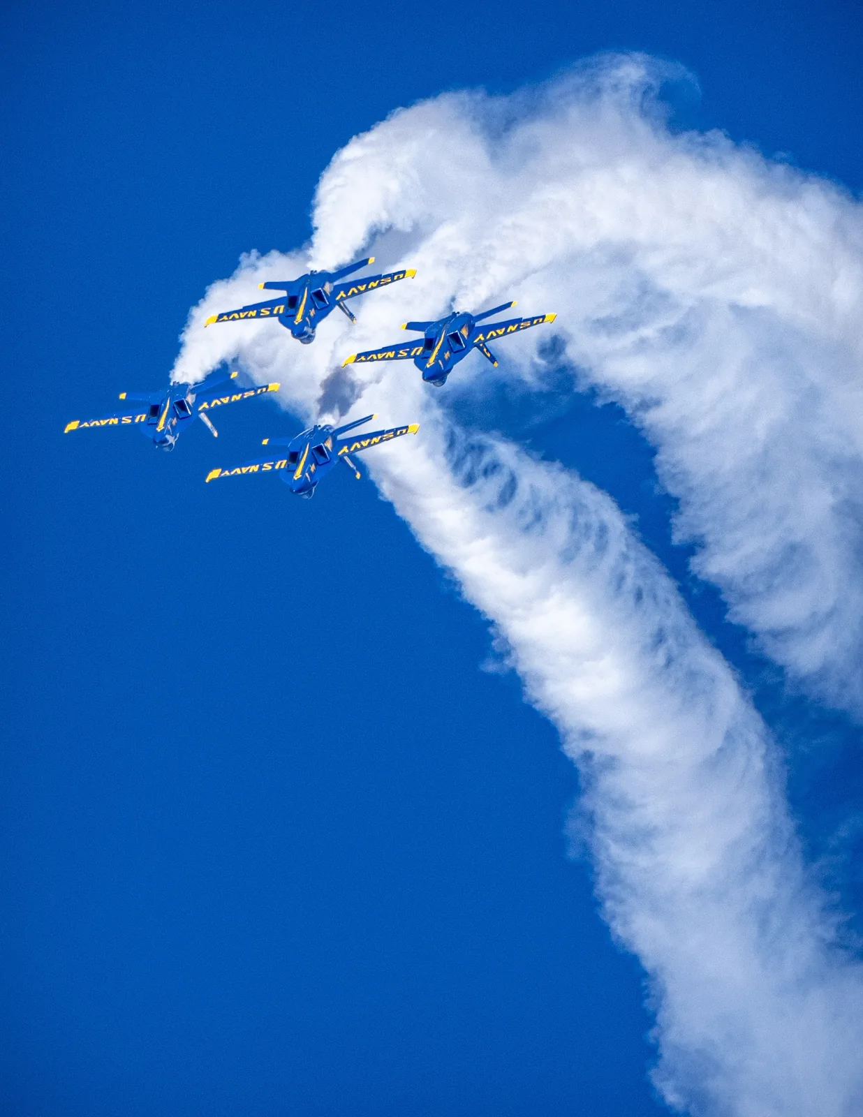 Blue Angels jets fly within a broad curved arc of white smoke.