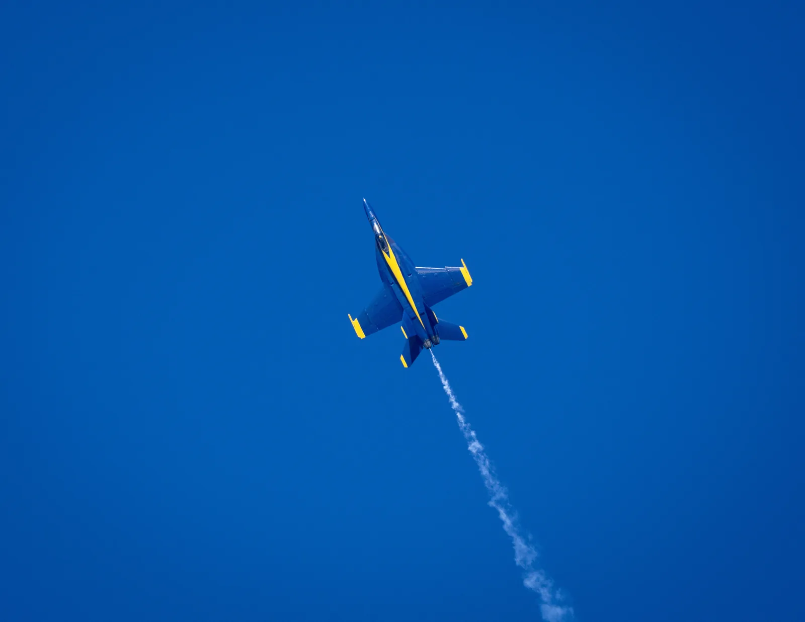A Blue Angels jet banks upward through blue sky.
