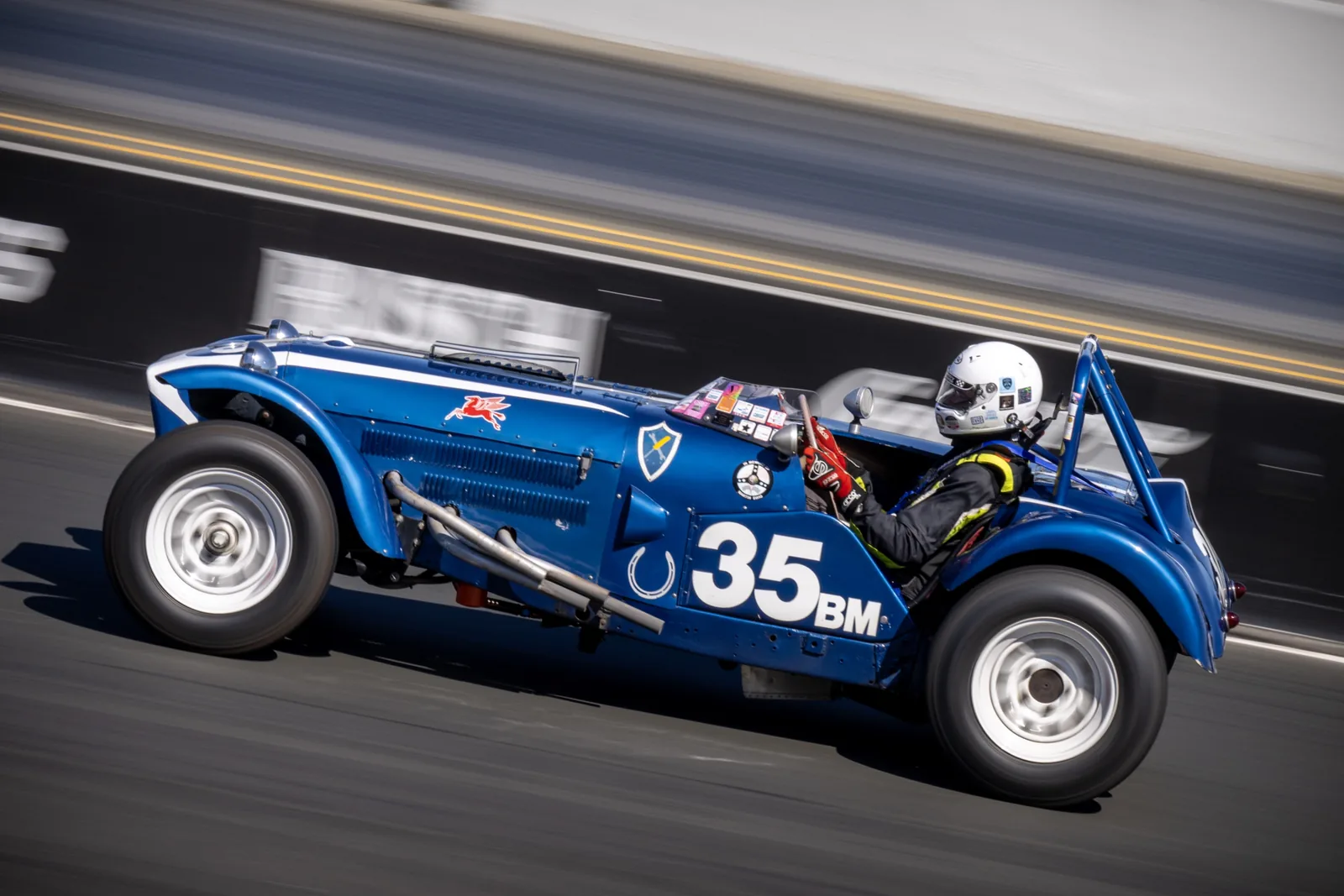A blue vintage racing car marked 35 speeds along a track with a helmeted driver; the background and road show strong motion blur.