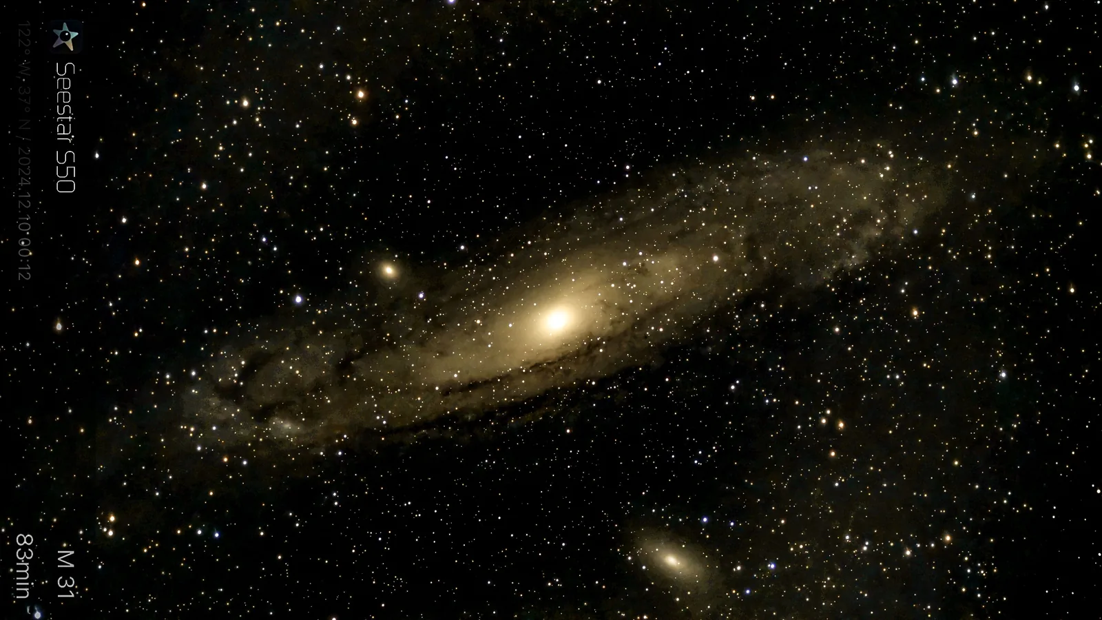 Spiral galaxy M31 stretches diagonally across a dense star field, with a smaller companion galaxy visible near the lower edge.