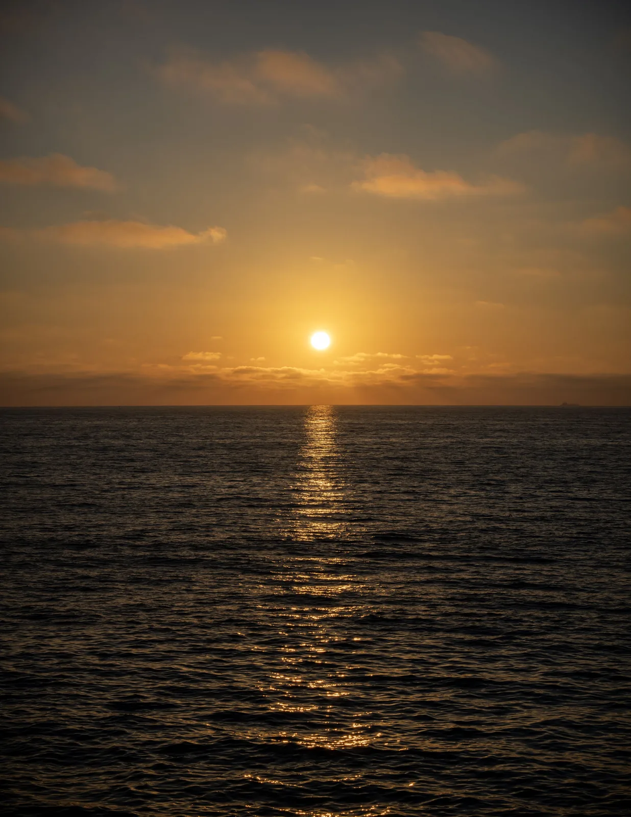 A low sun shines above the ocean, with a long golden reflection leading toward the foreground through rippling water.