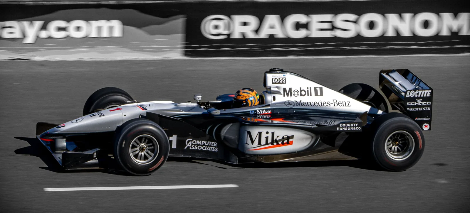 A silver-and-black open-wheel race car with Mercedes-Benz, Mobil 1, and large Mika lettering moves along a track.