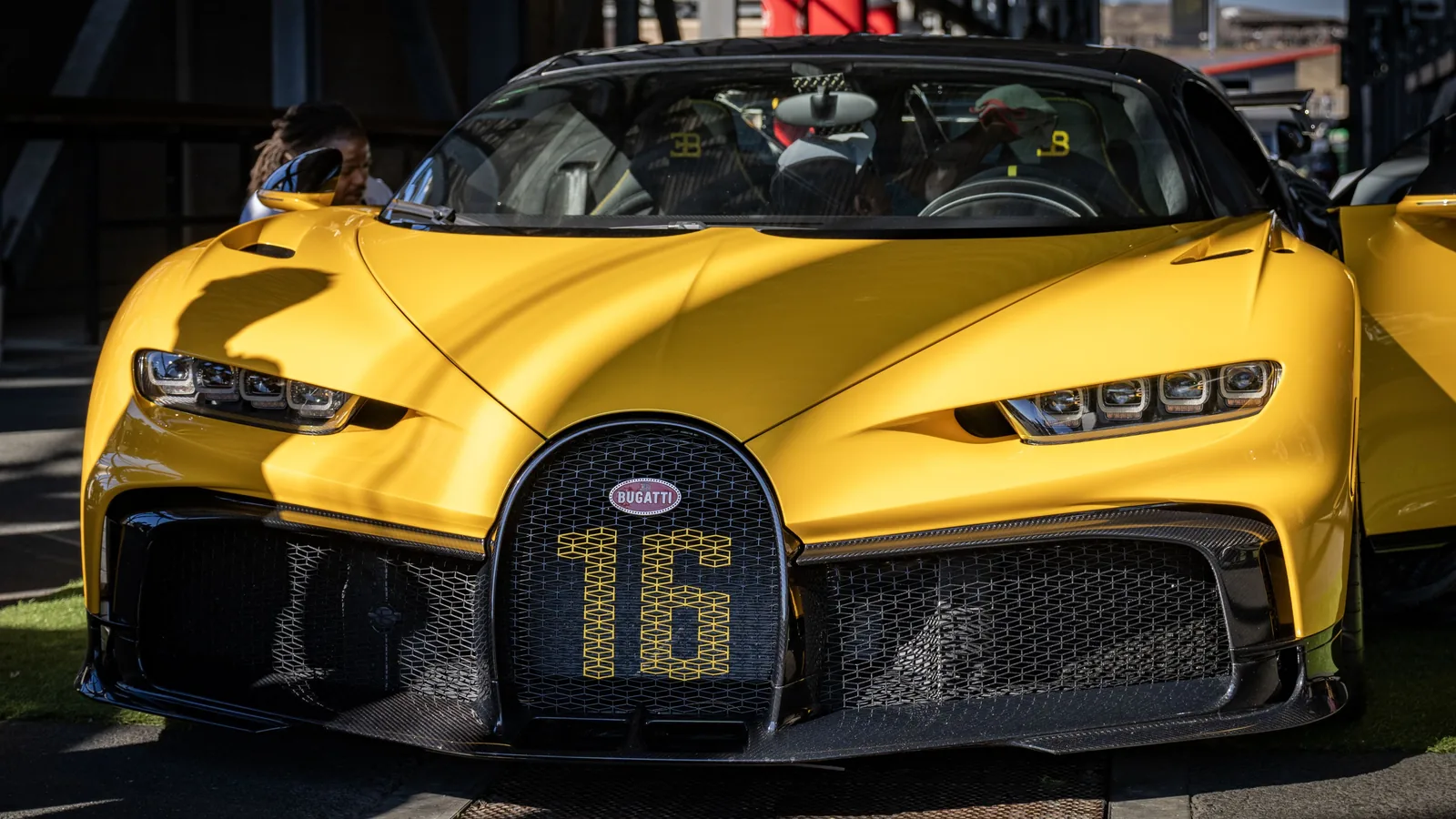 Front view of a yellow Bugatti Chiron with its grille, headlights, sculpted hood, and one door open.